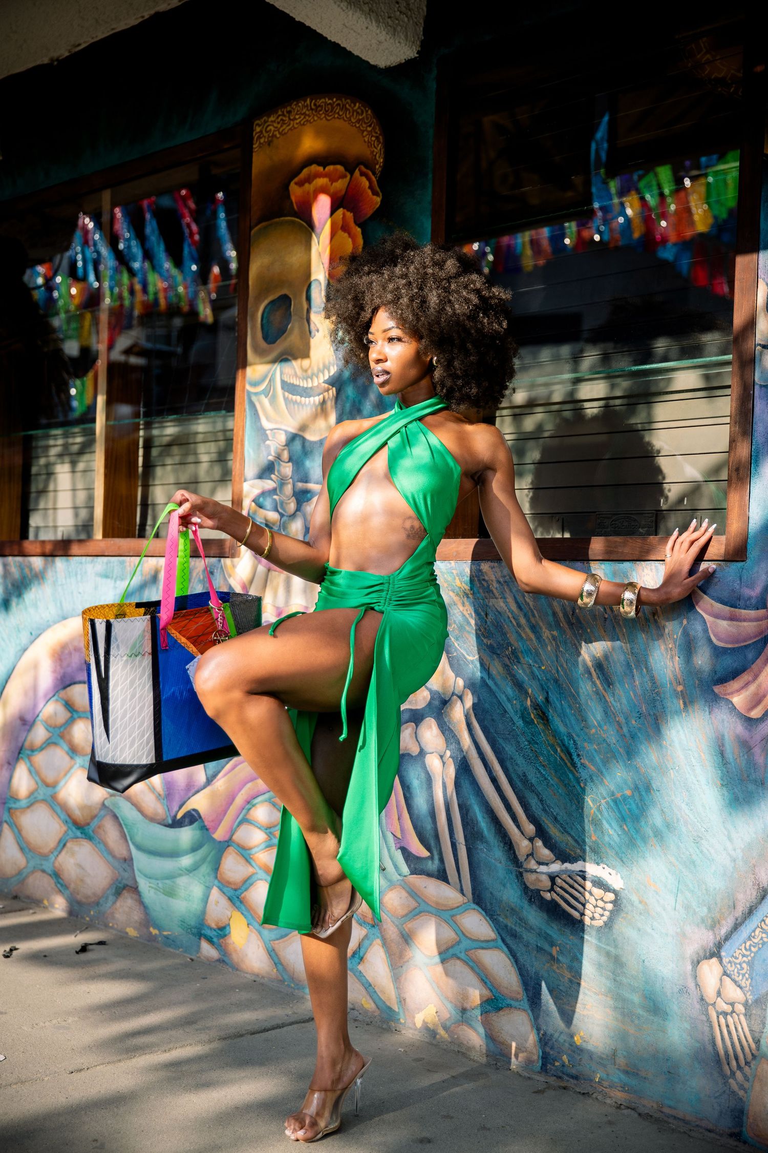A dancer in an emerald green dress poses gracefully against a colorful graffiti wall with shopping bags.