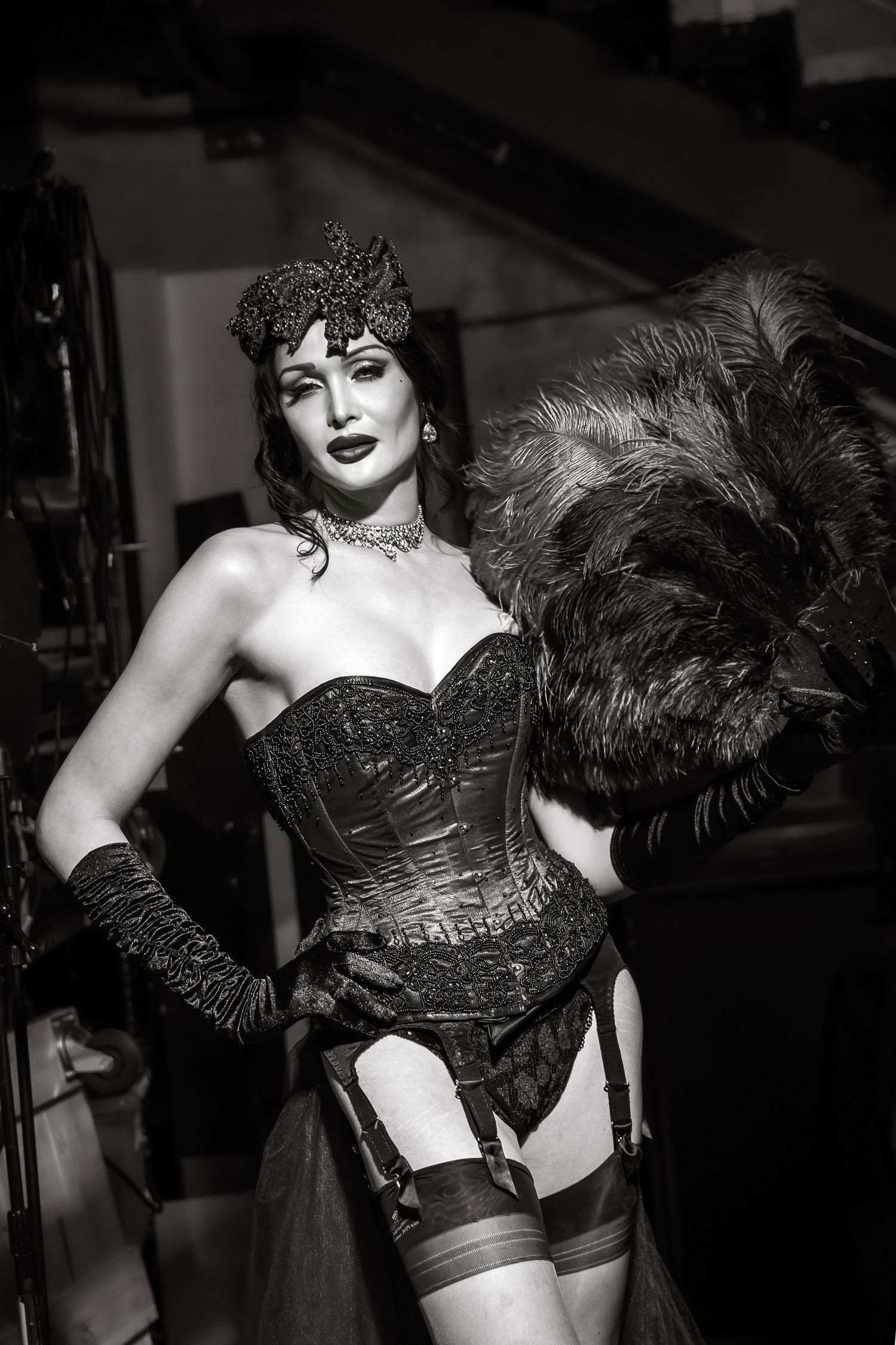 Black and white photo of a burlesque performer in a corset and feathers striking dramatic poses.