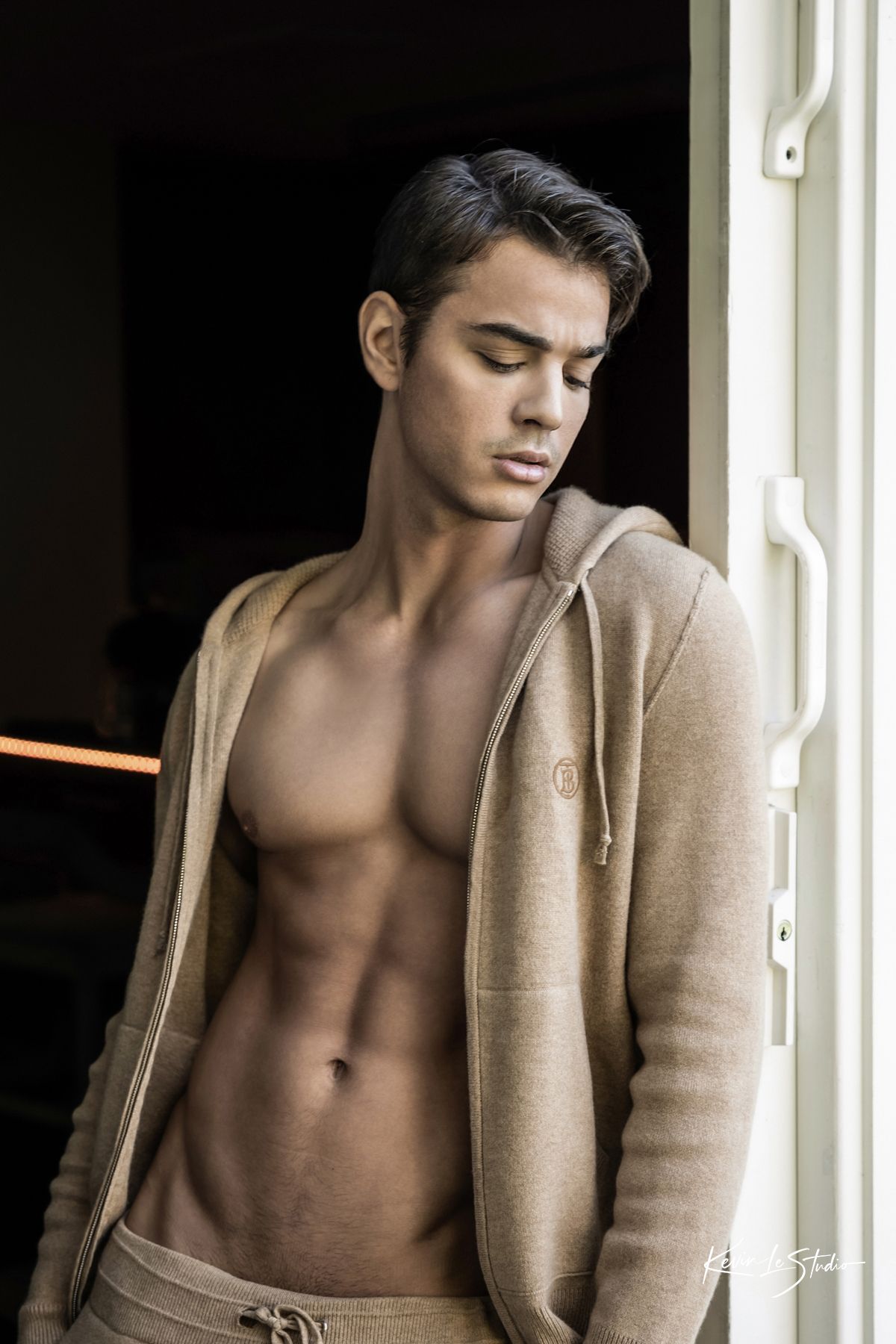 Fashion photo of a model wearing a beige cardigan against a window with dramatic lighting.