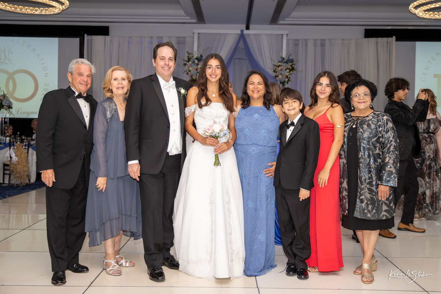 Guests in formal attire pose together at an elegant event in a room with modern circular lighting fixtures.