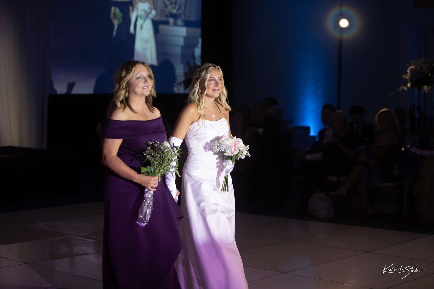 Wedding party dances under blue lighting at an evening reception celebration.