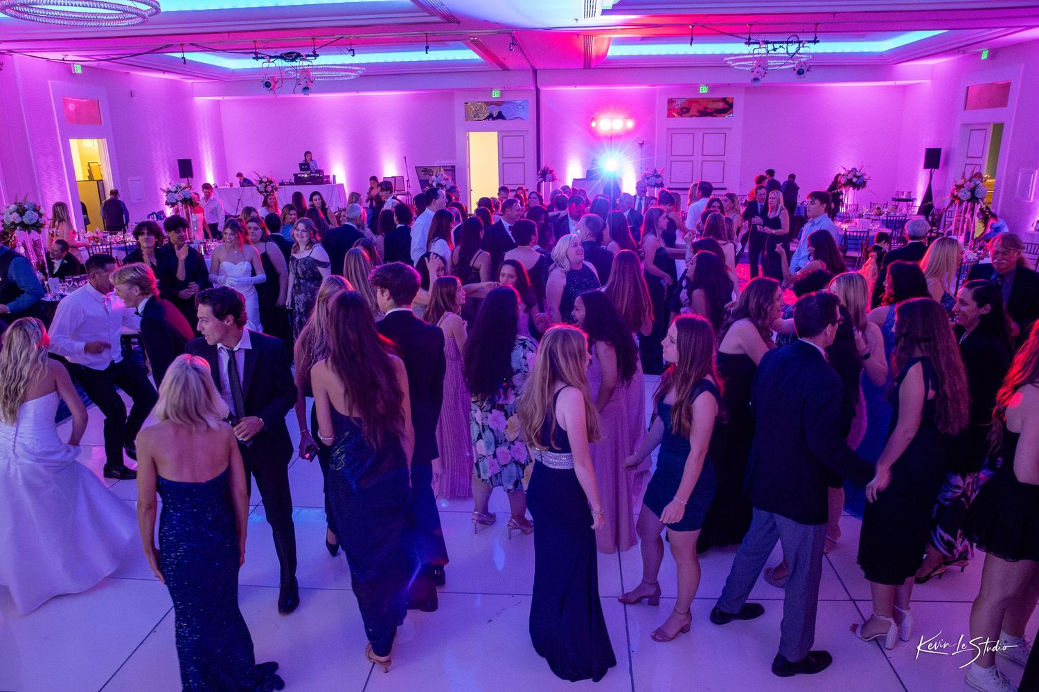 People dancing at a large indoor event with purple and pink lighting illuminating the dance floor.