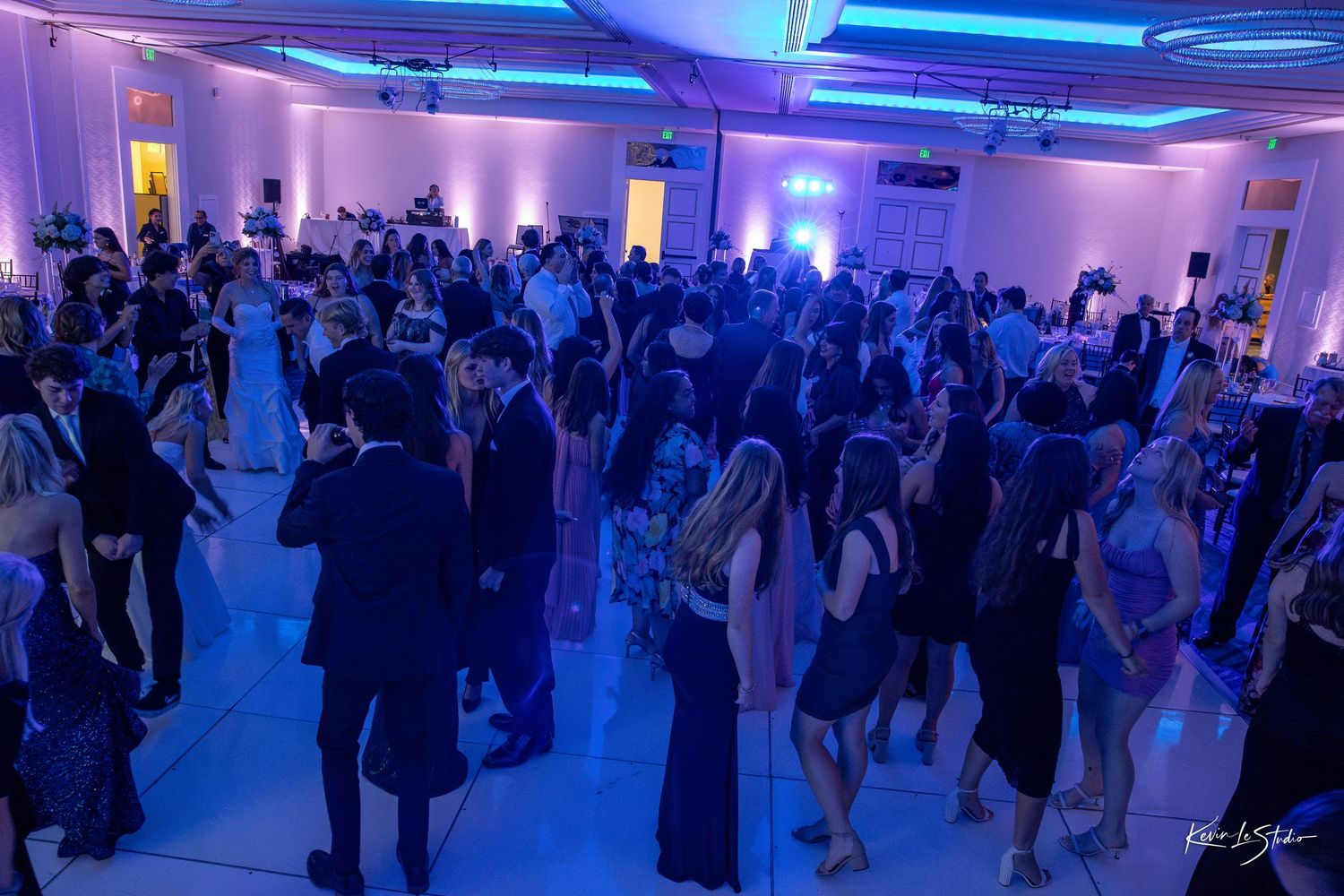 A large crowd gathers in a ballroom illuminated with vibrant blue lighting for a social event or dance party.