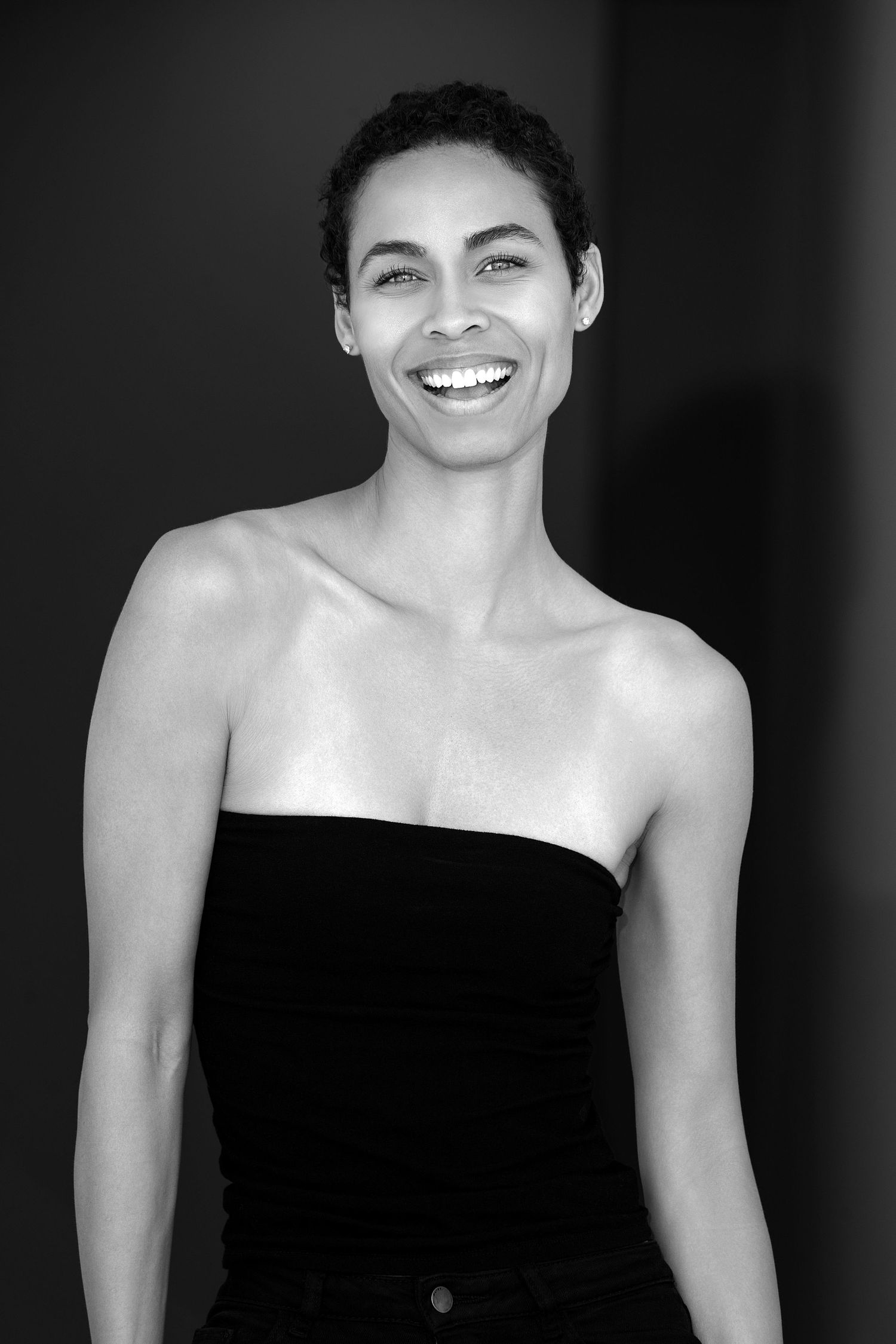 Black and white portrait series showing joyful expressions and a strapless black top against dark background.