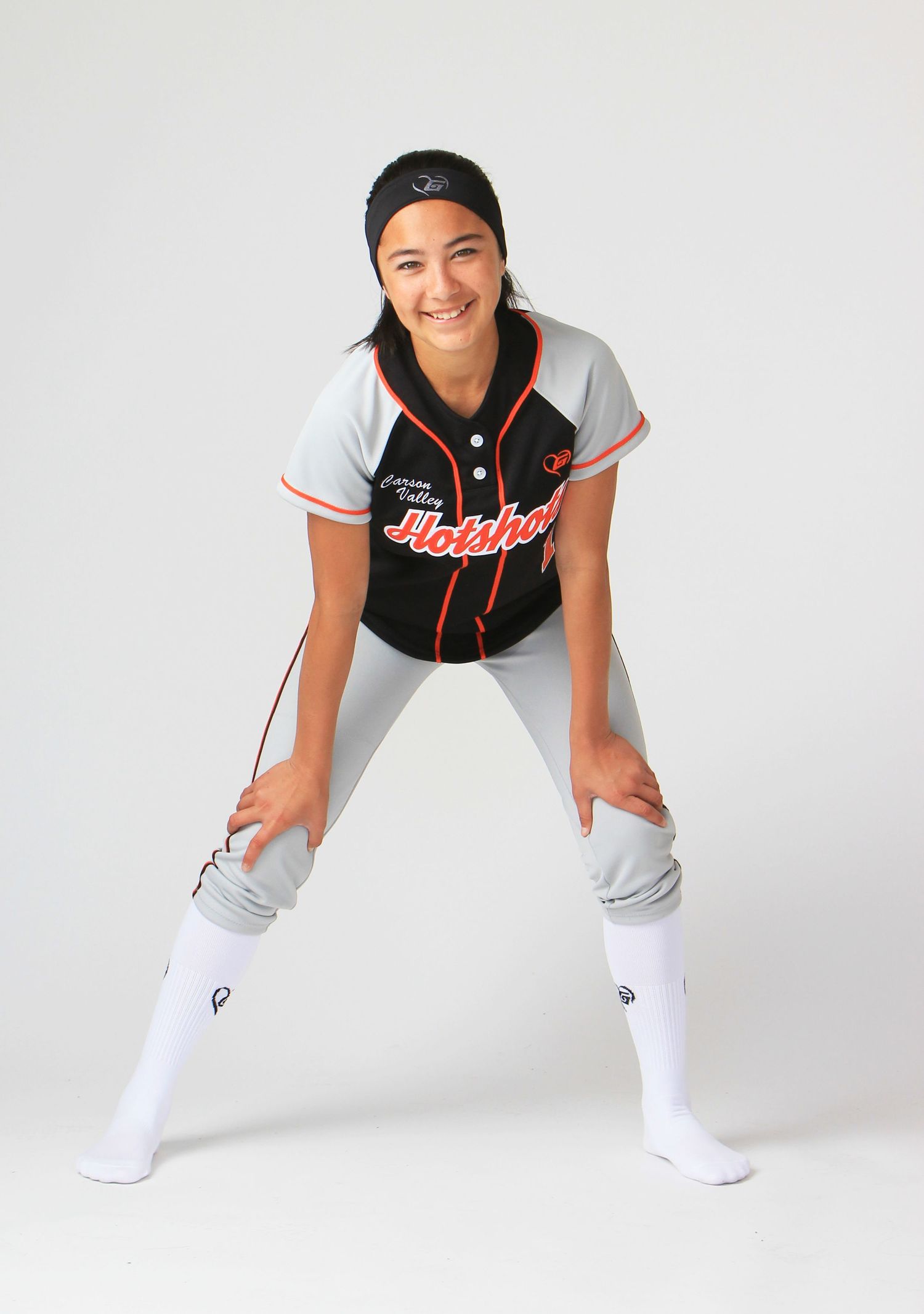 Baseball player in black and gray uniform with white socks poses in ready stance position against white background.
