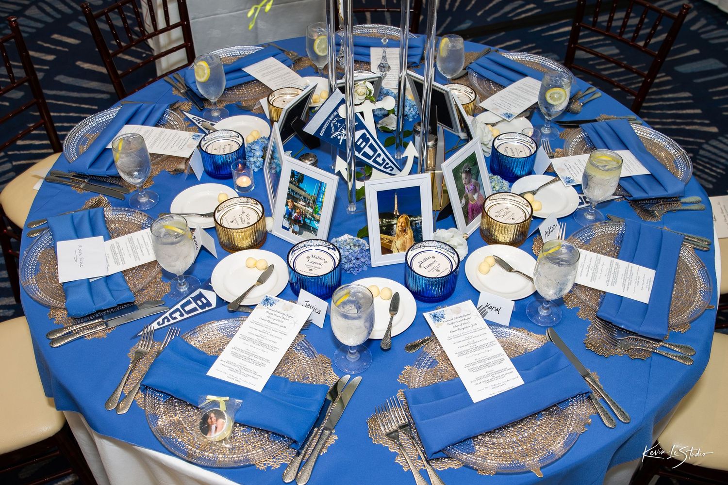 Multiple round tables decorated in blue and white with place settings and centerpieces for a formal dinner event.