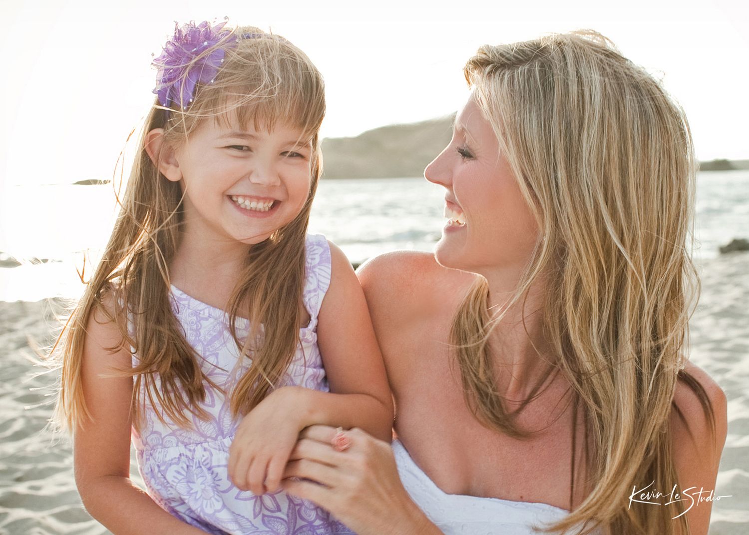 A laughing mother and young daughter share a joyful moment together on a sunny beach.