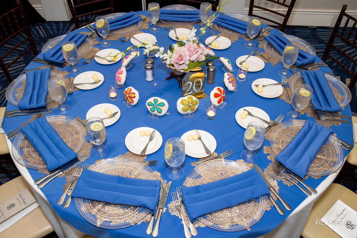 Round dining table set with blue tablecloth and elegant place settings for a formal dinner party.