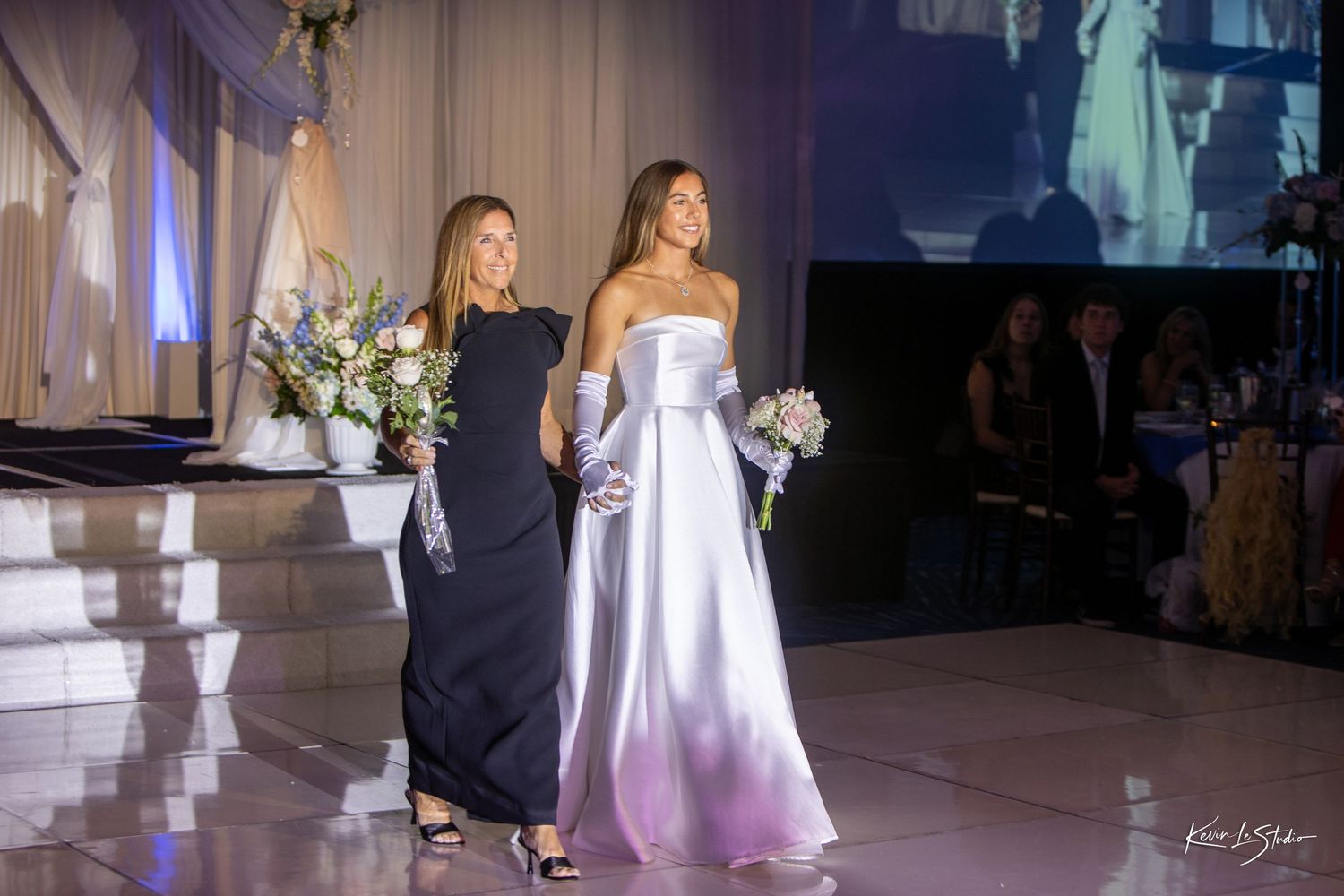 Wedding couple shares their first dance together in an elegant ballroom with dramatic lighting and decor.