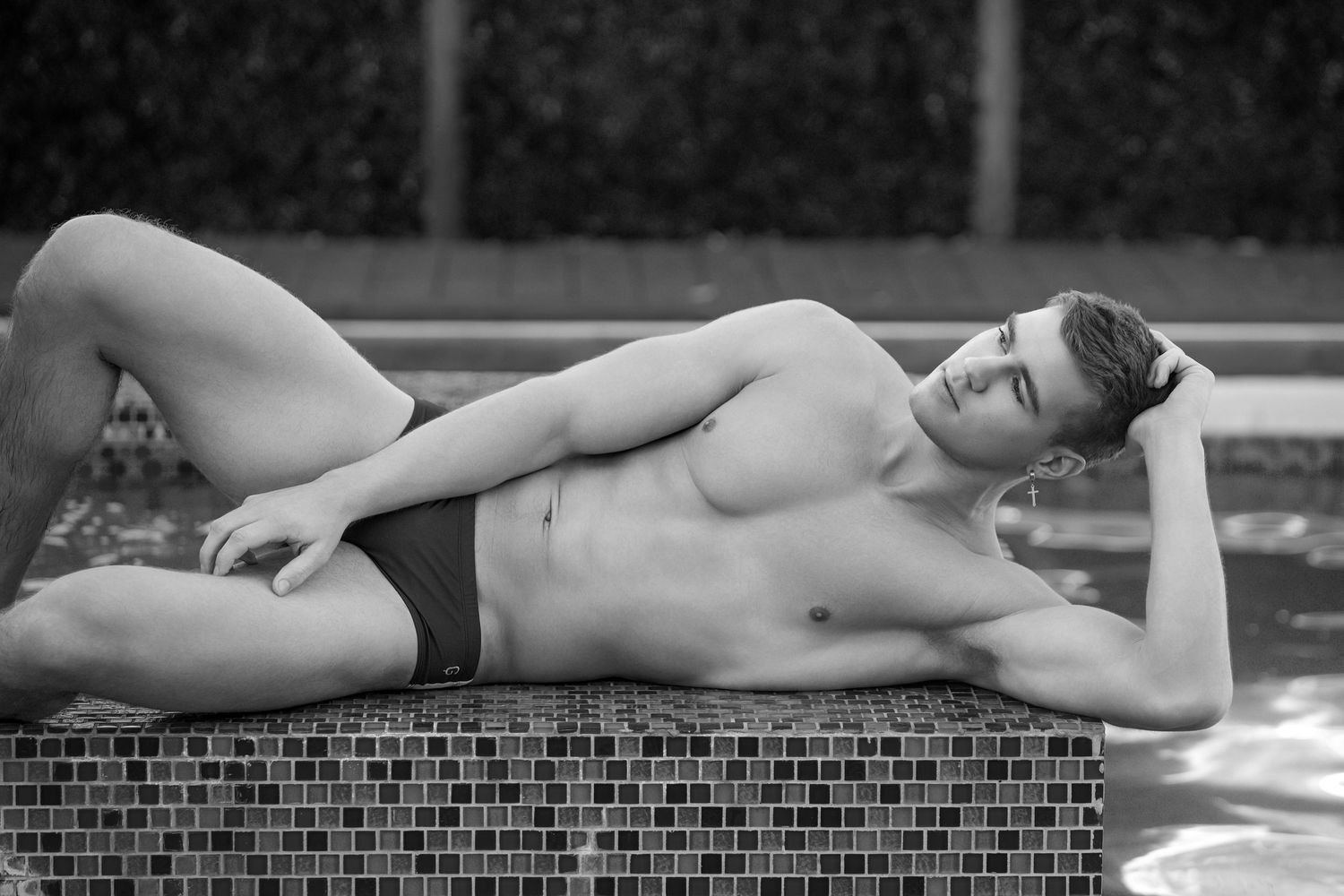 A black and white photo series showing a person reclining on a brick wall near a swimming pool.