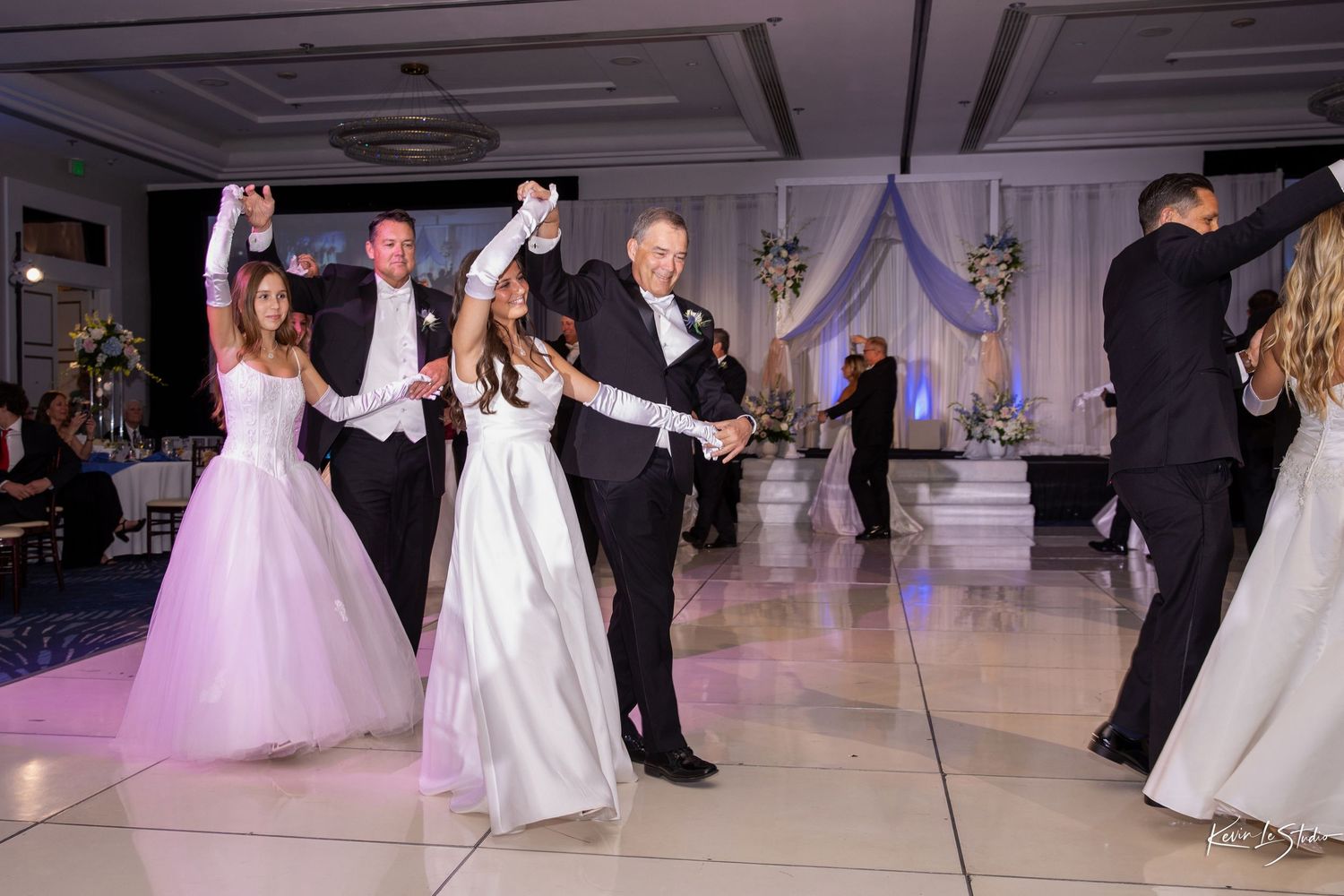 Couples dancing together at an elegant wedding reception with white and purple decor in a ballroom.