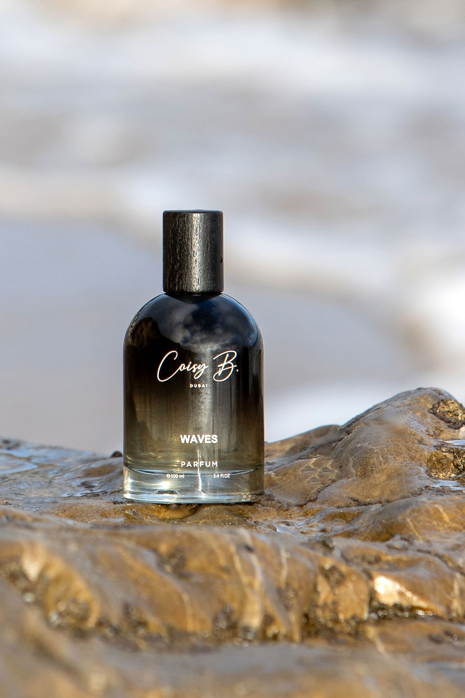 A black perfume bottle labeled 'Waves' sits on a textured gold metallic surface in soft focus.