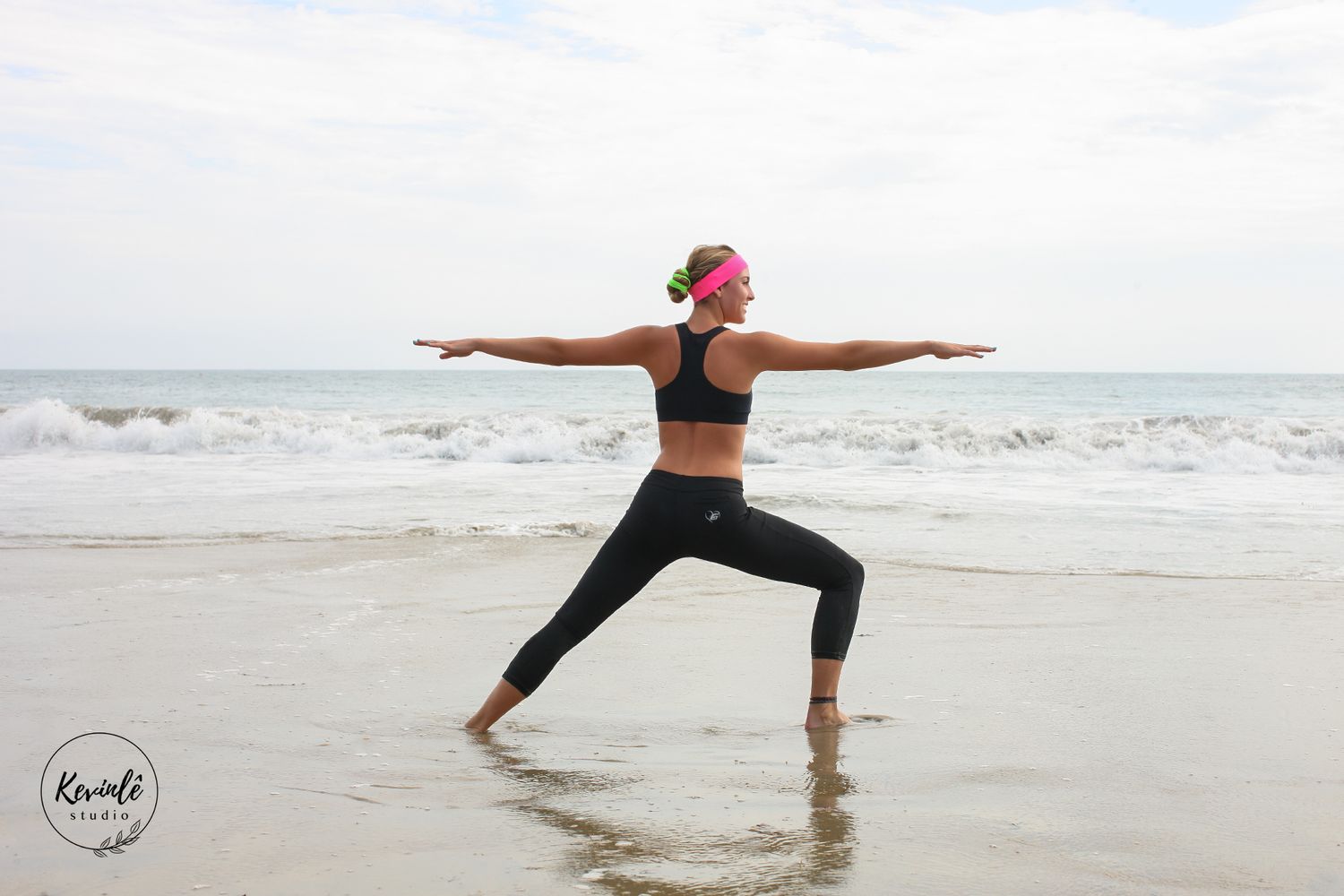 Person performs yoga warrior pose on beach at sunset with waves crashing in background.