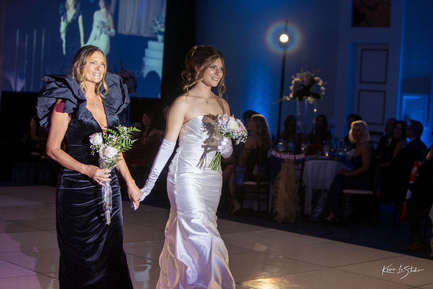 Dancers move gracefully on a dimly lit dance floor illuminated by blue lighting during an elegant evening event.