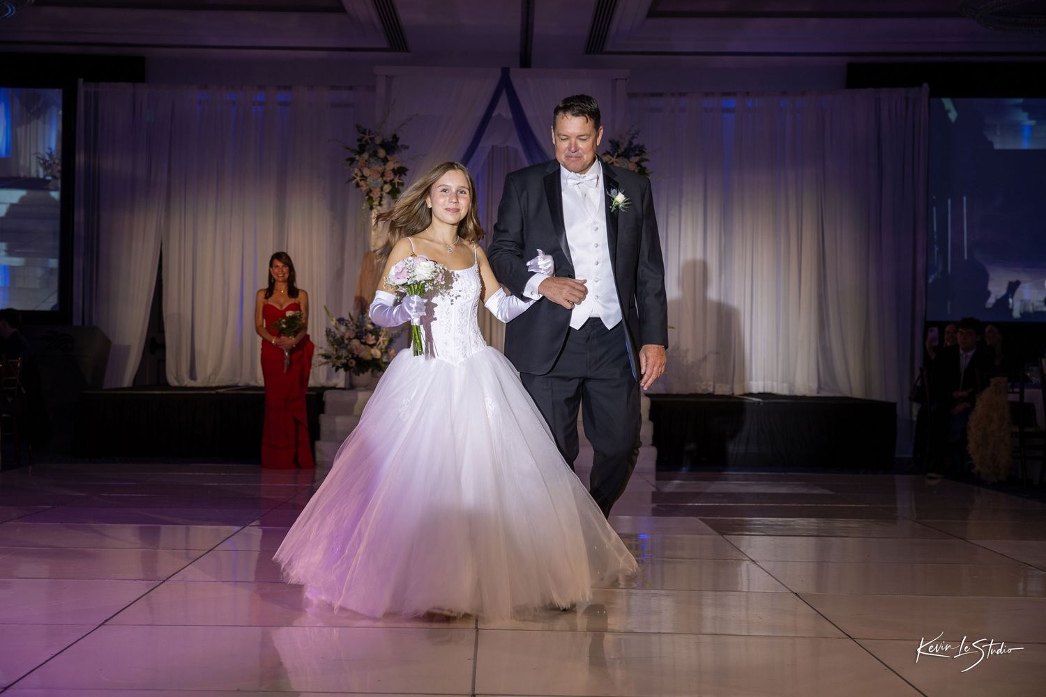 A couple shares their first dance at a wedding reception with a white ballgown and black tuxedo on an illuminated dance floor.