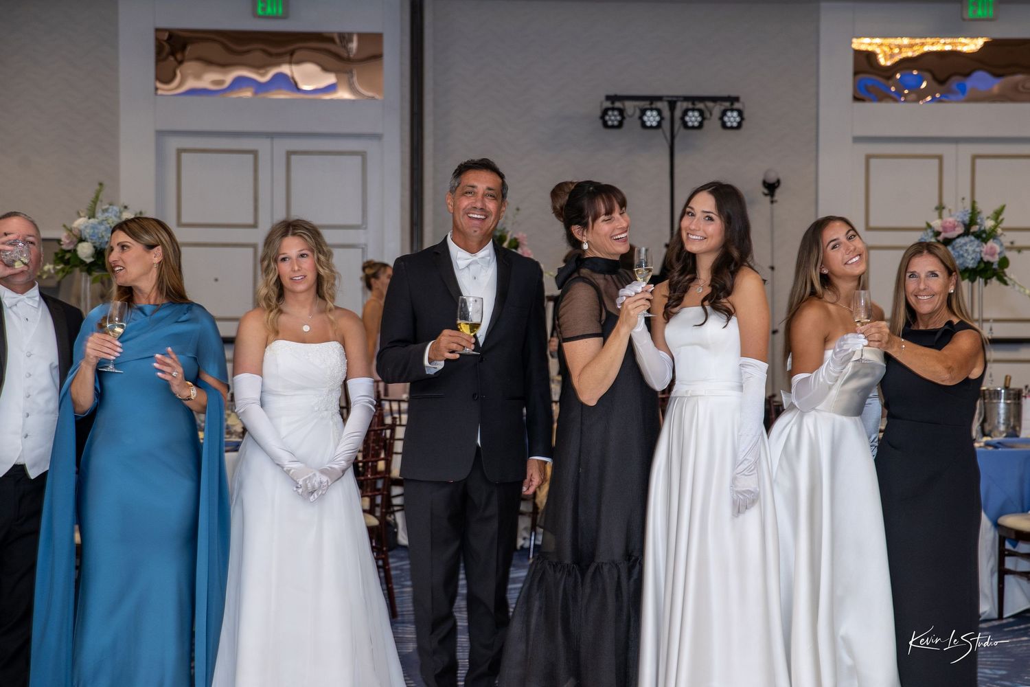 Wedding party members in formal attire stand together holding drinks during a reception celebration.