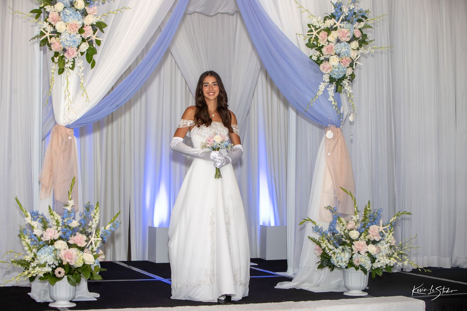 A wedding dress display with white gowns and floral arrangements against a grey backdrop with purple lighting accents.
