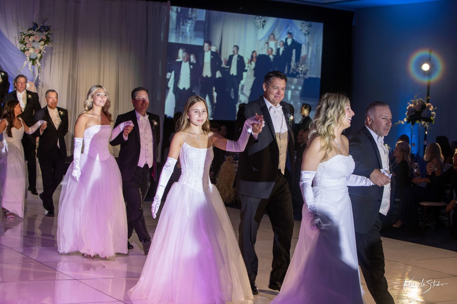 Couples dancing together at an elegant wedding reception with soft pink and blue lighting on the dance floor.