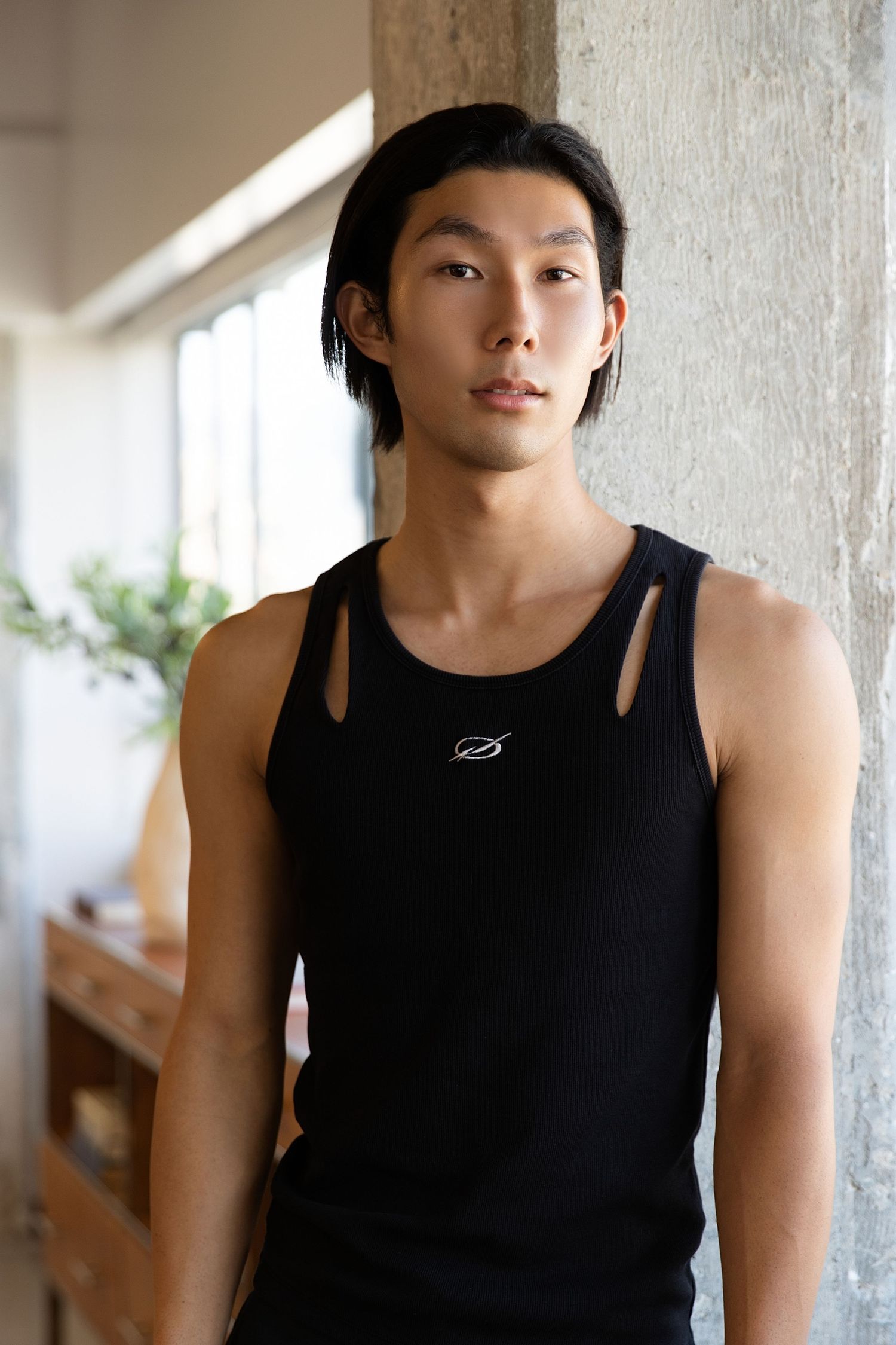 Person in black tank top poses against concrete wall in series of four similar portraits.