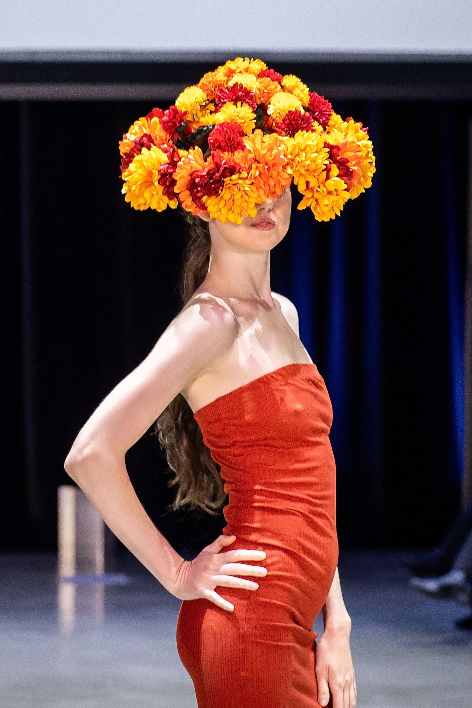 A person in a red strapless dress poses on stage wearing a vibrant orange and yellow floral headpiece.