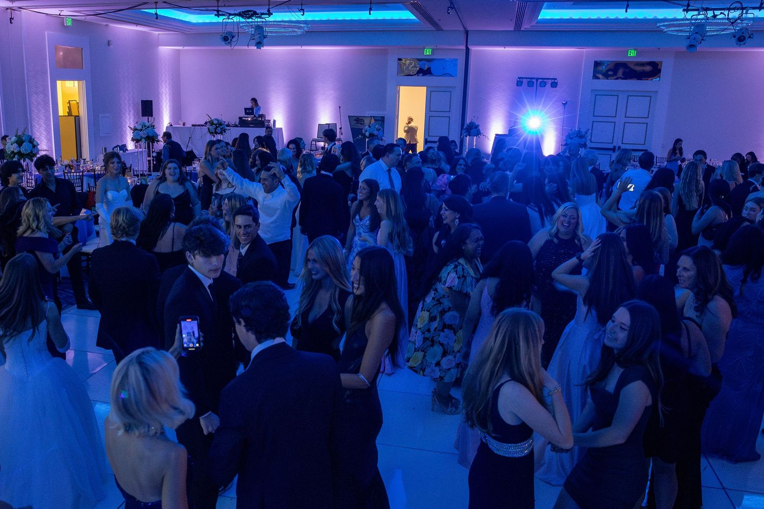 A crowded dance floor illuminated by blue and purple lighting at an indoor event venue.