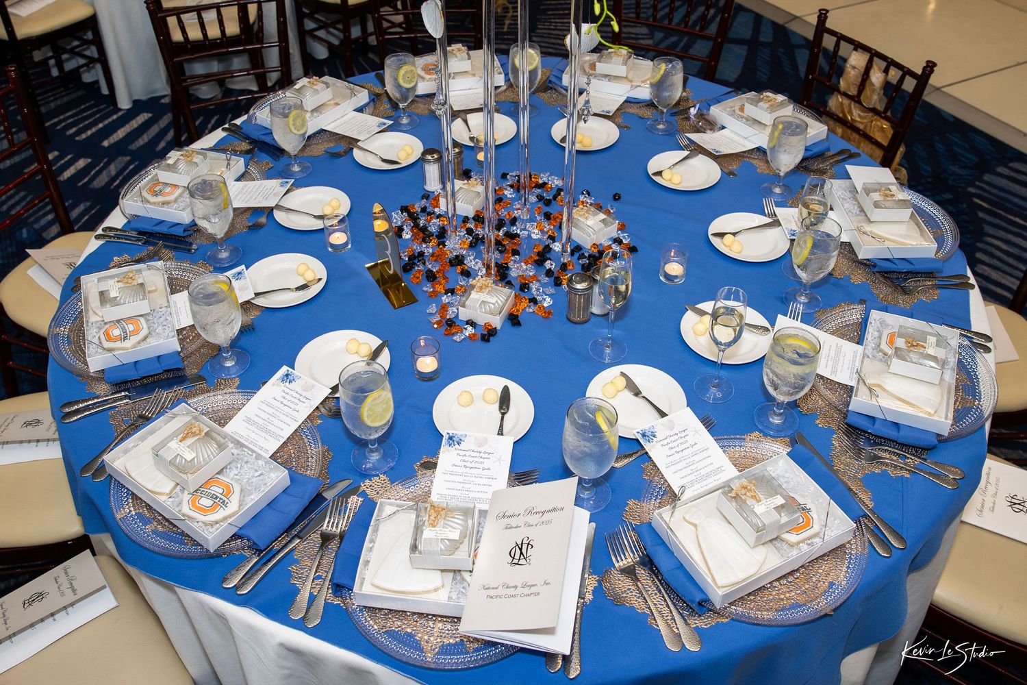 A formal dining table with bright blue tablecloth set with white plates, silverware and centerpieces for an elegant event.