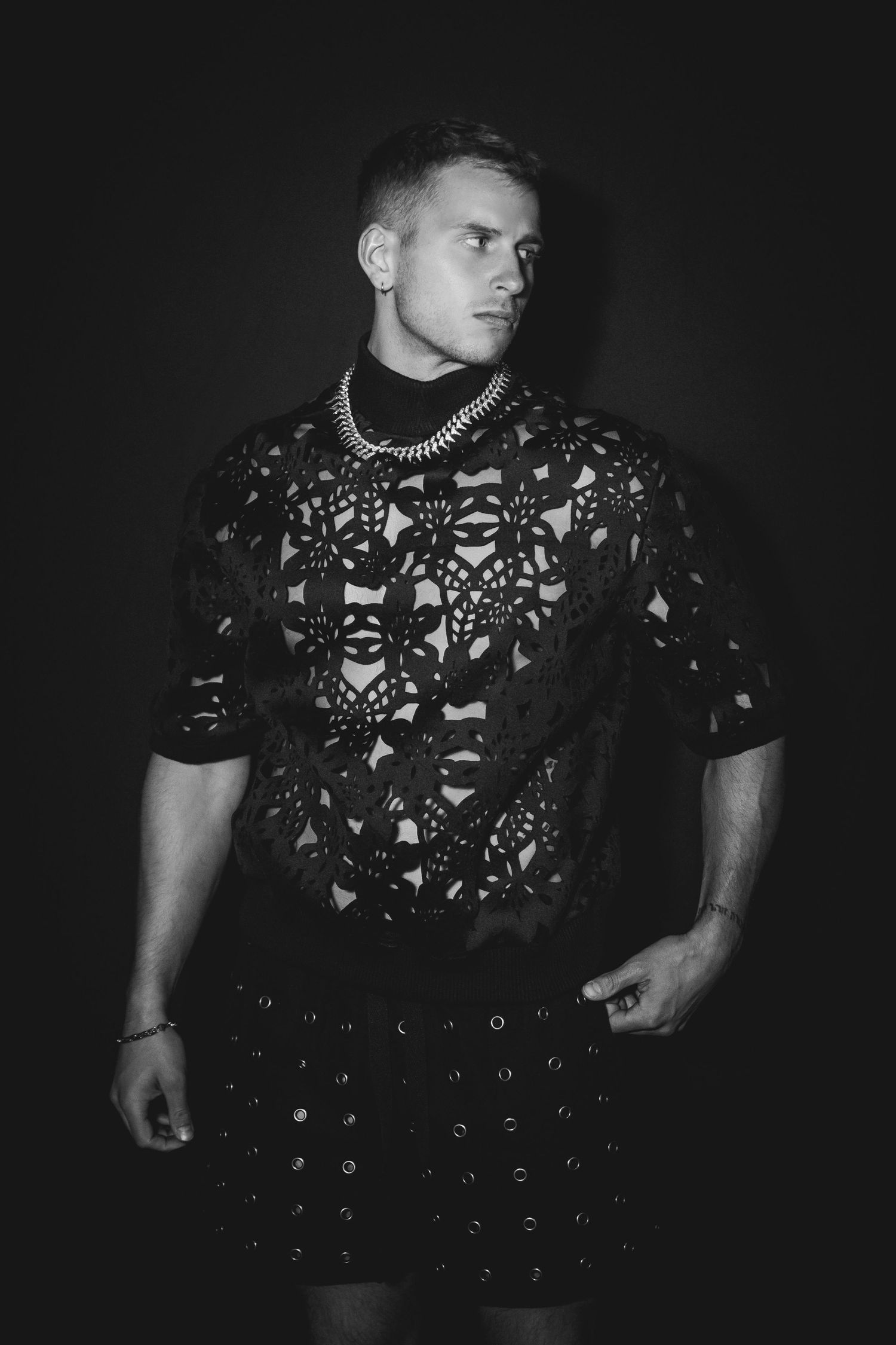 A dramatic black and white fashion portrait showing someone wearing an edgy studded and patterned dark outfit.
