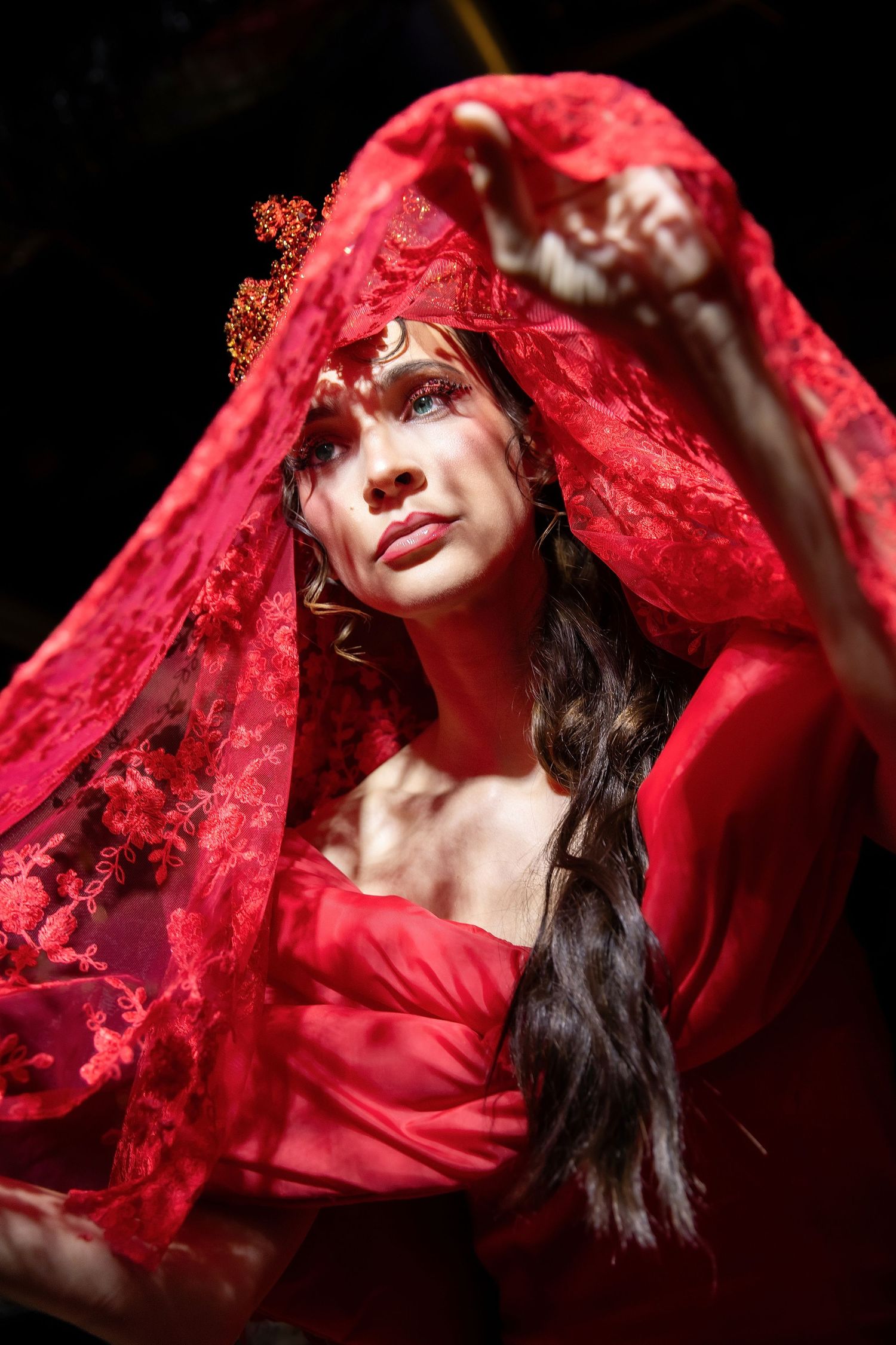 A dramatic artistic portrait featuring flowing red fabric and lace against a dark background.