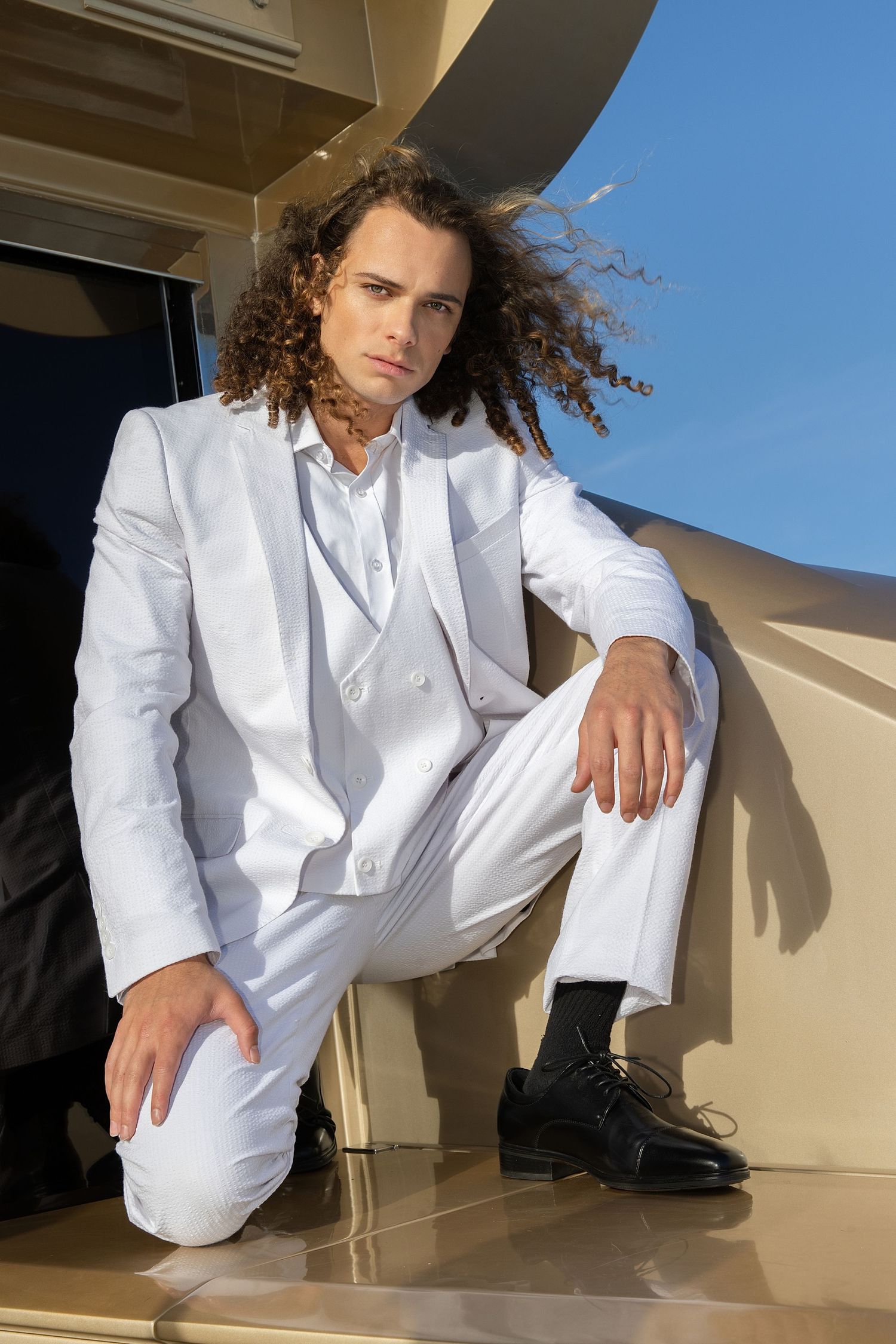 Person in all-white suit poses in dramatic angles against architectural backdrop during golden hour lighting.