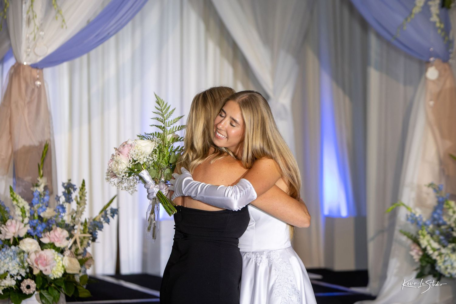 A couple shares a tender moment during a wedding reception with blue lighting and floral decorations.
