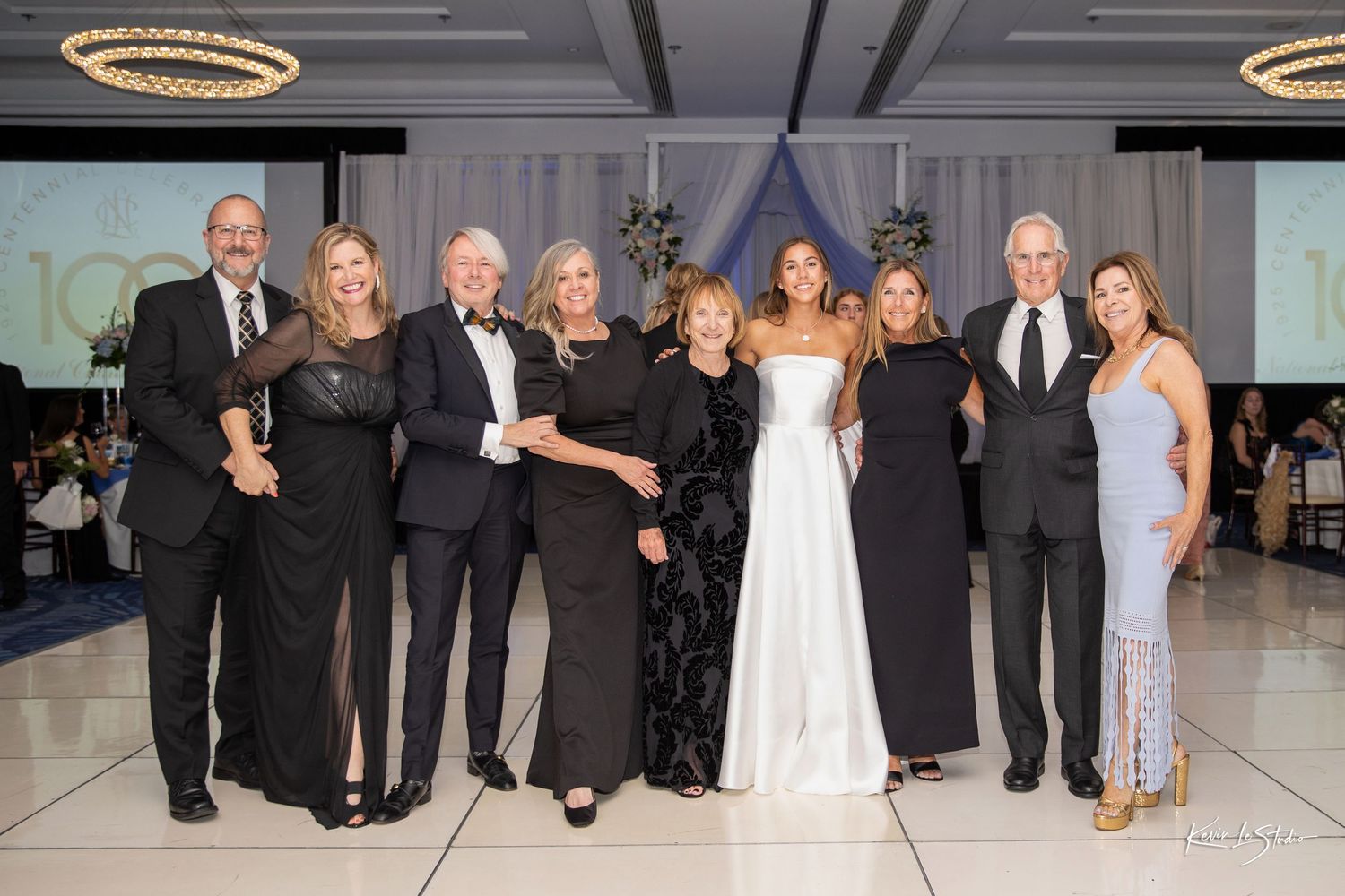 Wedding party members dance together on an elegant ballroom floor during an evening reception celebration.