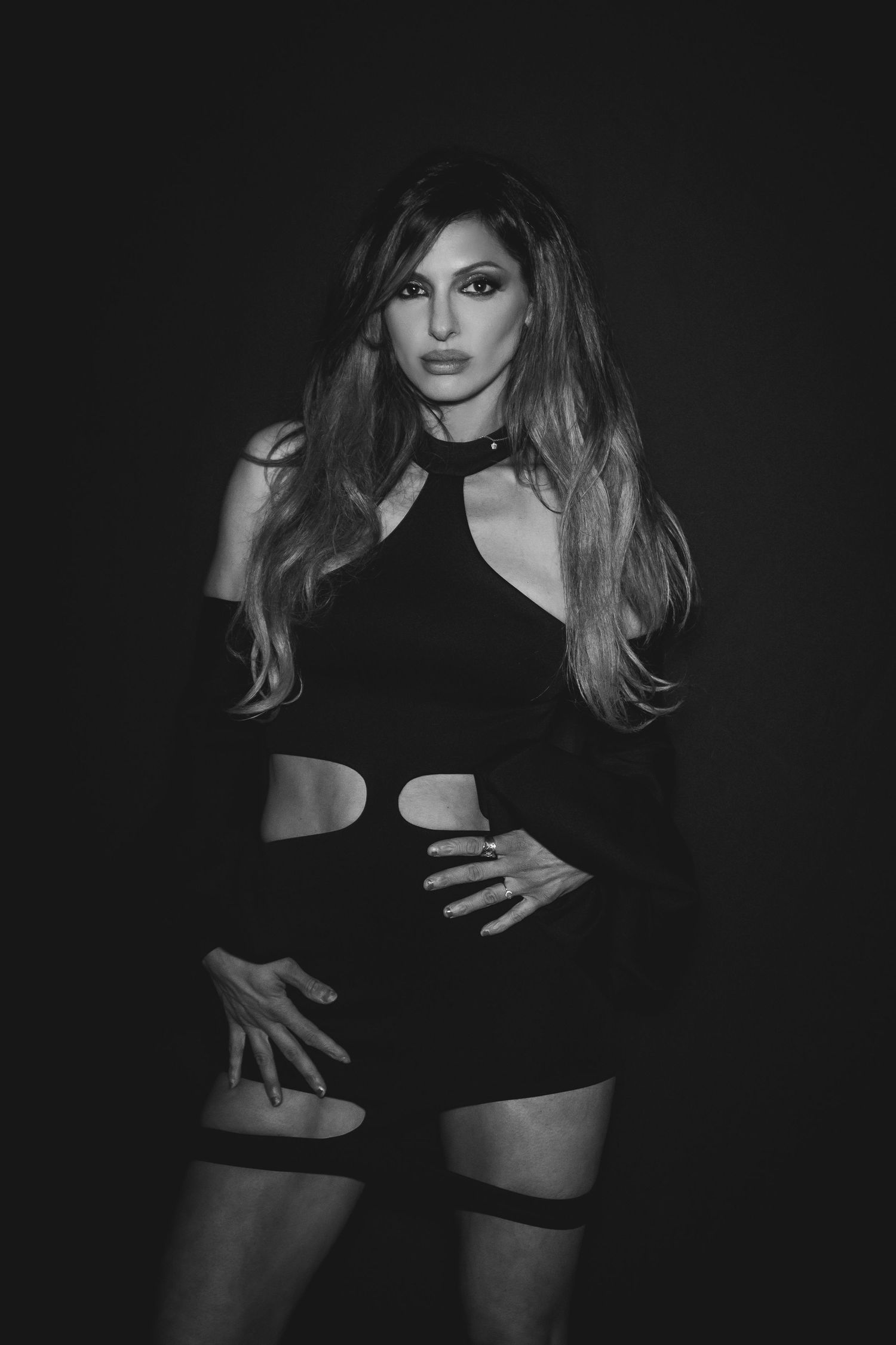 Dramatic black and white fashion photos showing a model in dark clothing posing against a black background.