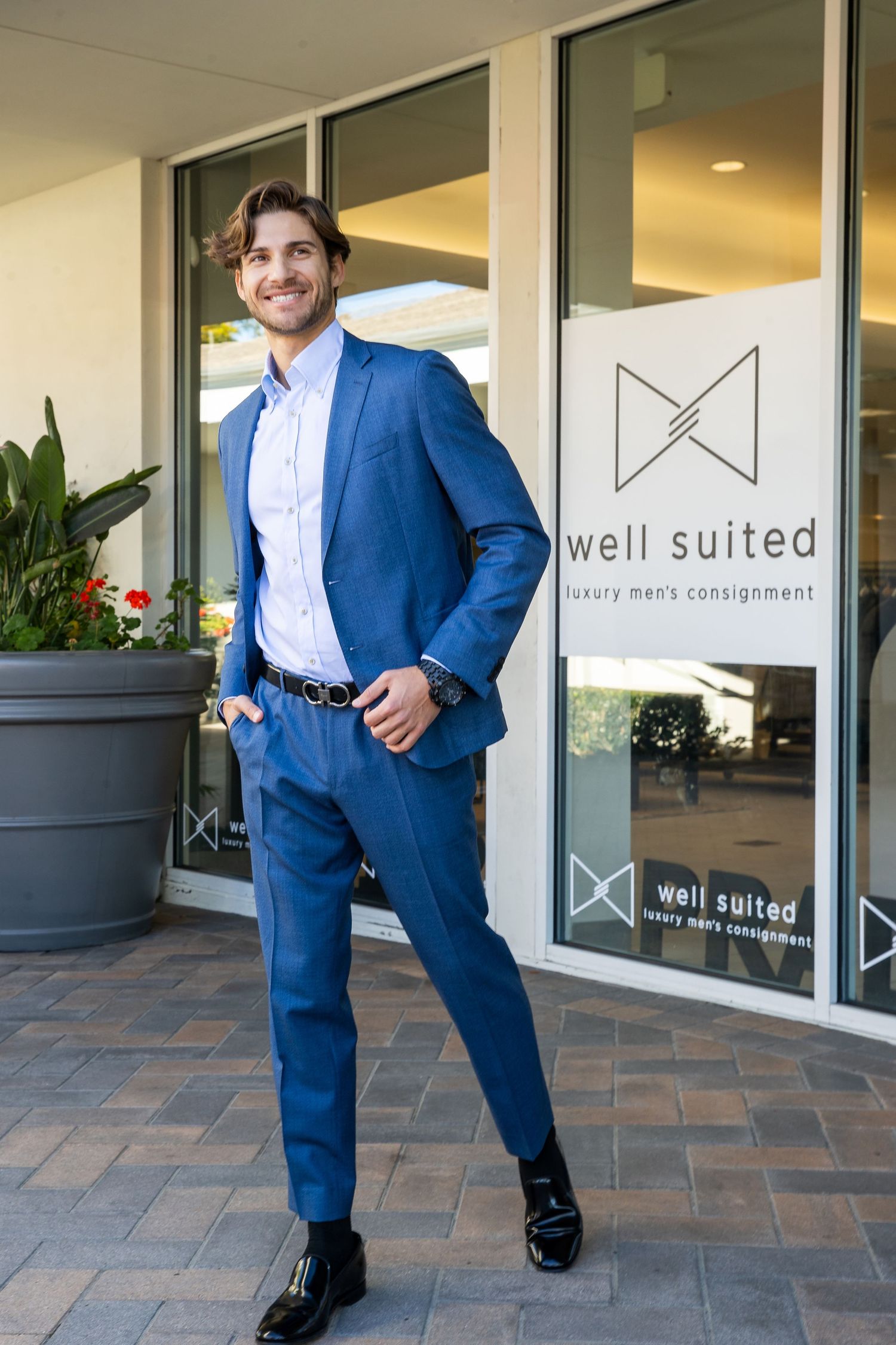 Professional in a navy blue suit poses in front of a storefront with 'well suited' signage on the windows.