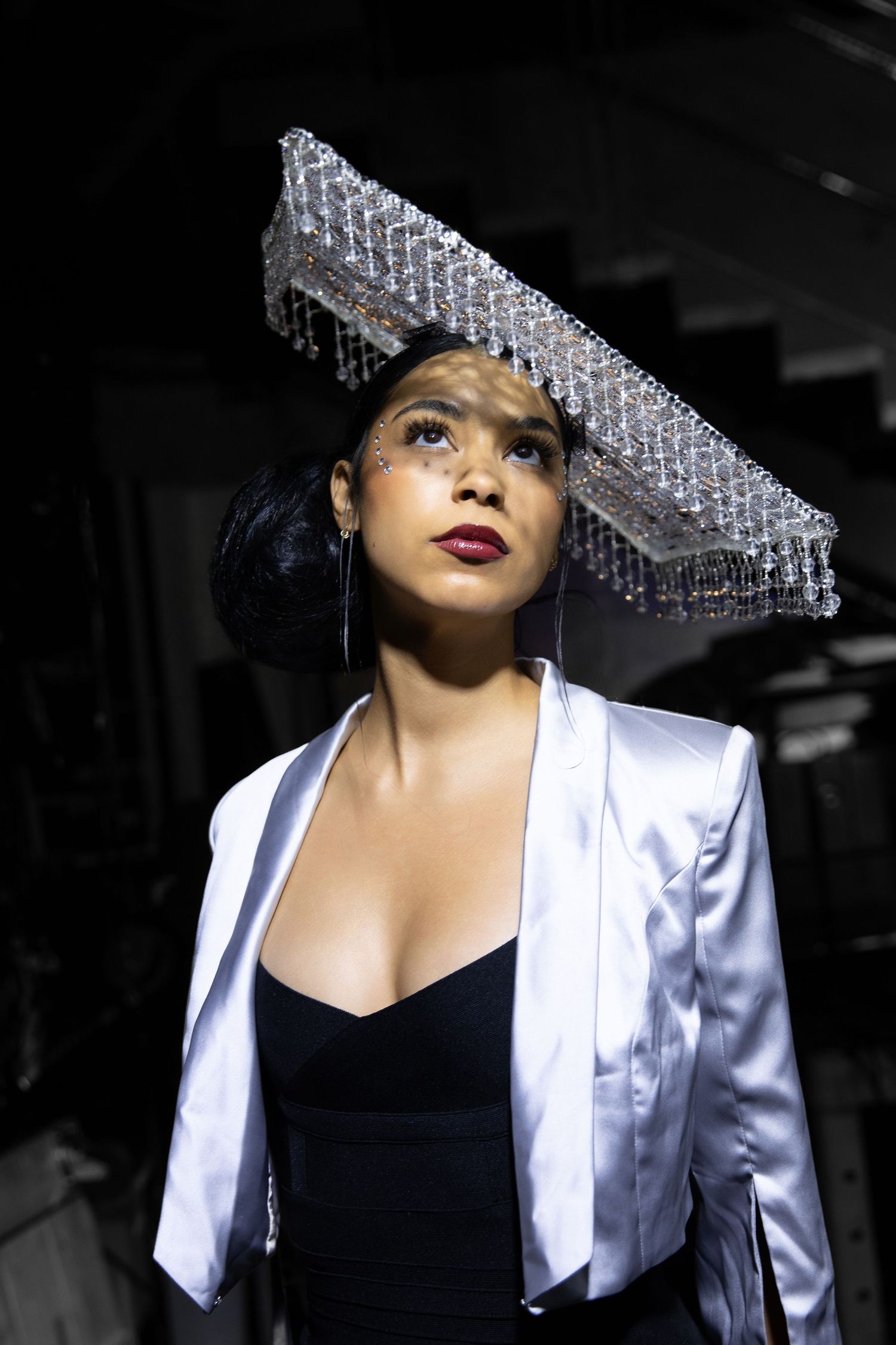 A glamorous portrait series featuring a white satin blazer and crystal-adorned hat against a dark background.