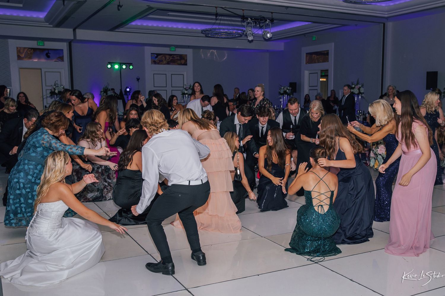 Panoramic view of people dancing and celebrating at a formal event in a ballroom with purple lighting.