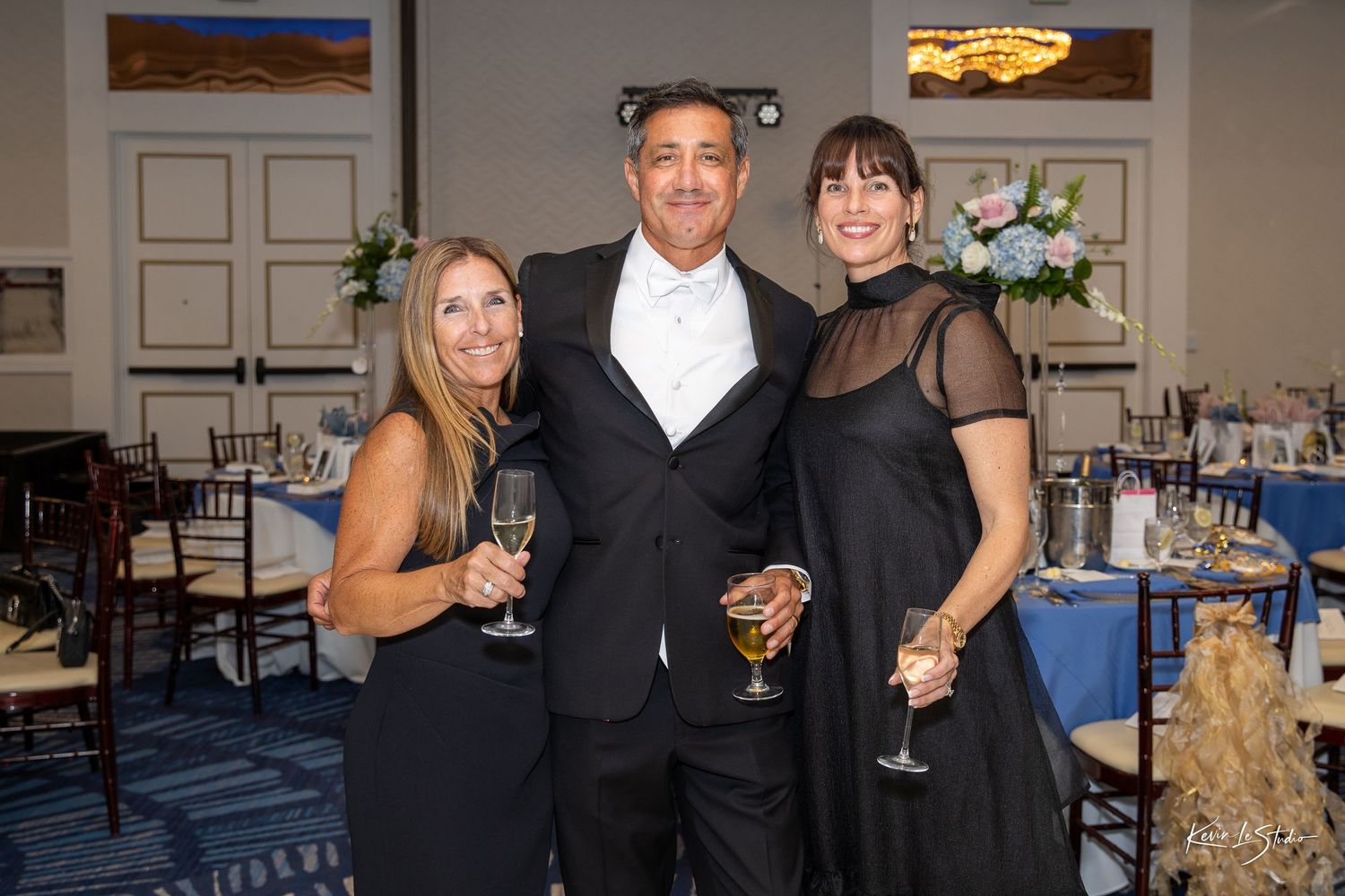 People enjoying drinks and socializing at an elegant evening reception with blue decor and table settings.