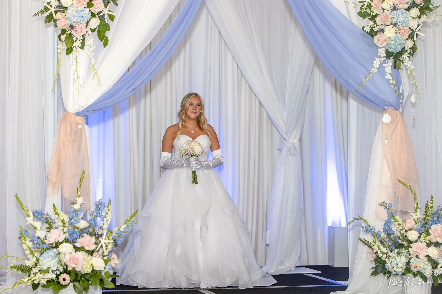A wedding venue decorated with white and blue draped fabric, floral arrangements, and elegant lighting for a romantic ceremony.