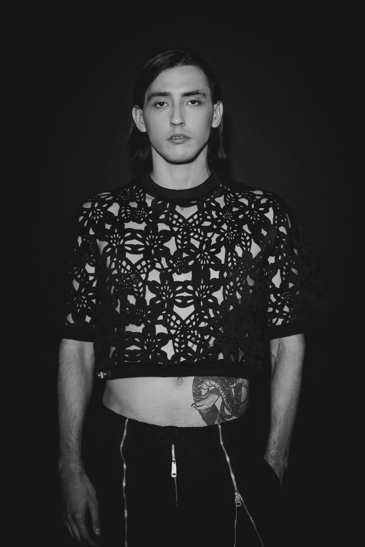 Black and white photo of person wearing a cropped patterned sweater with geometric designs against dark background.