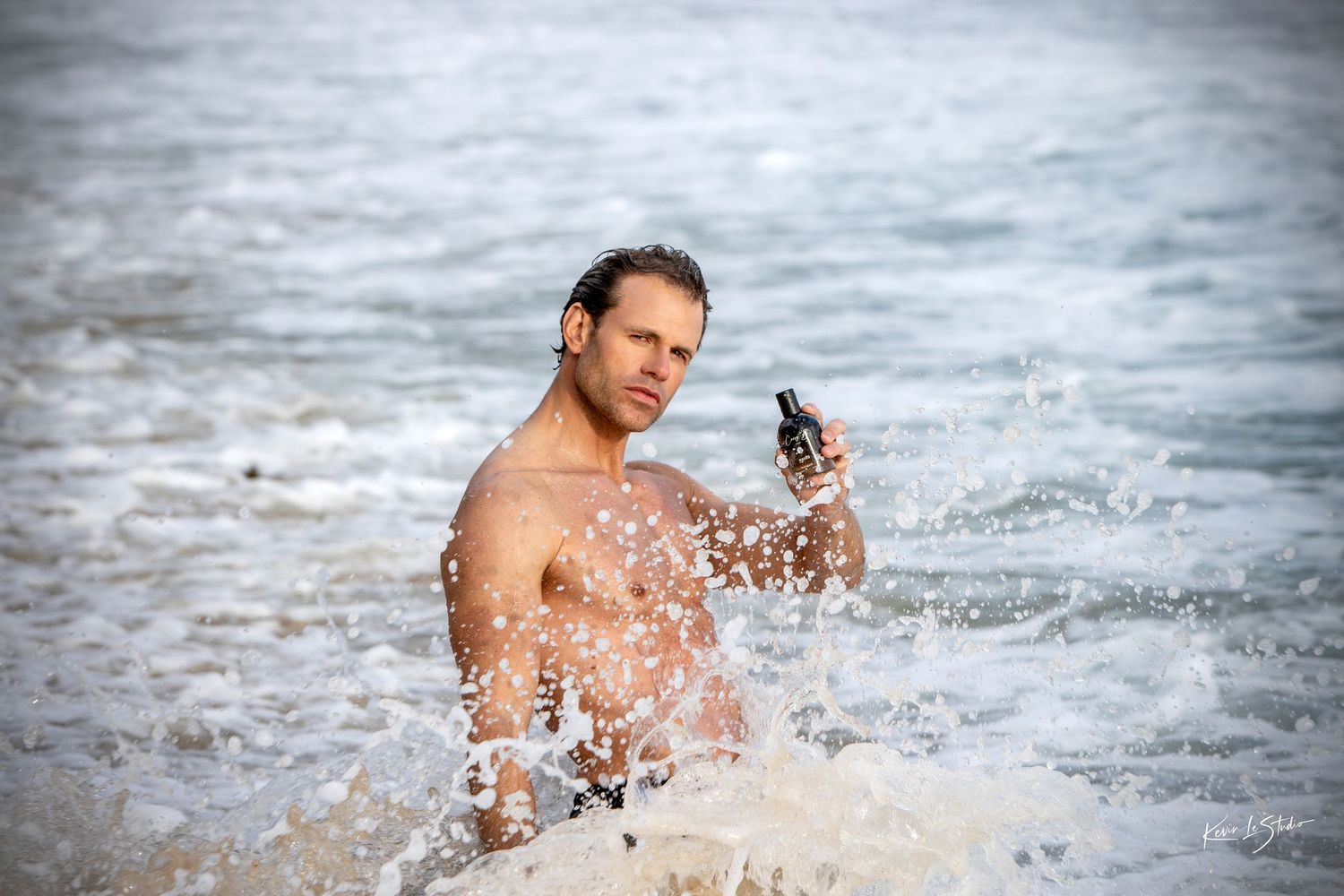 Person splashing and playing in ocean waves while holding a phone camera on a sunny day.