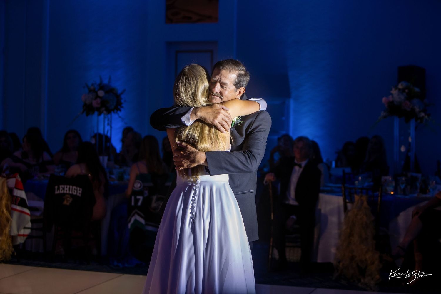 A romantic couple embraces during their first dance at a wedding reception with dramatic blue lighting.