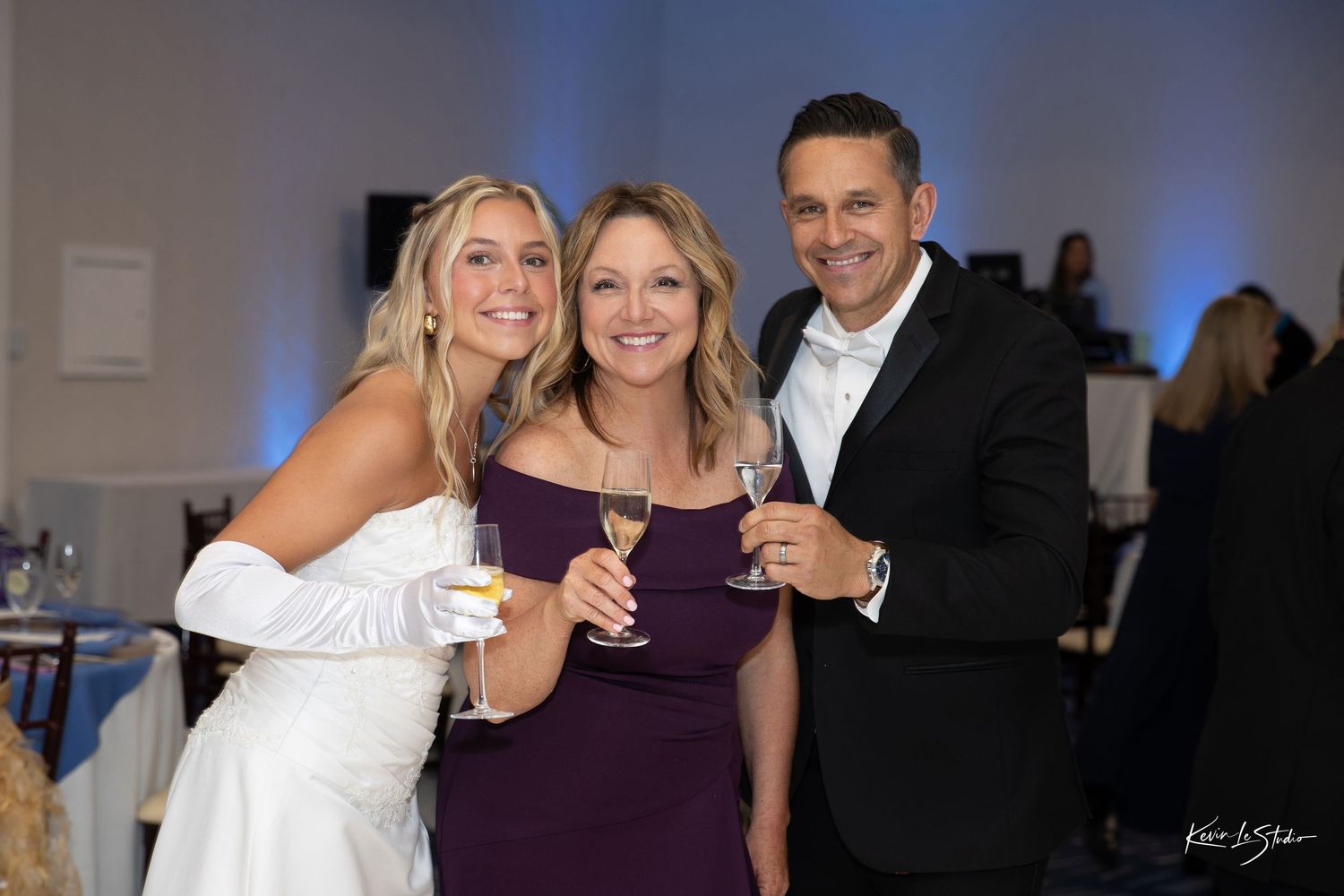 A group of people in formal attire pose together at an event with blue lighting in the background.