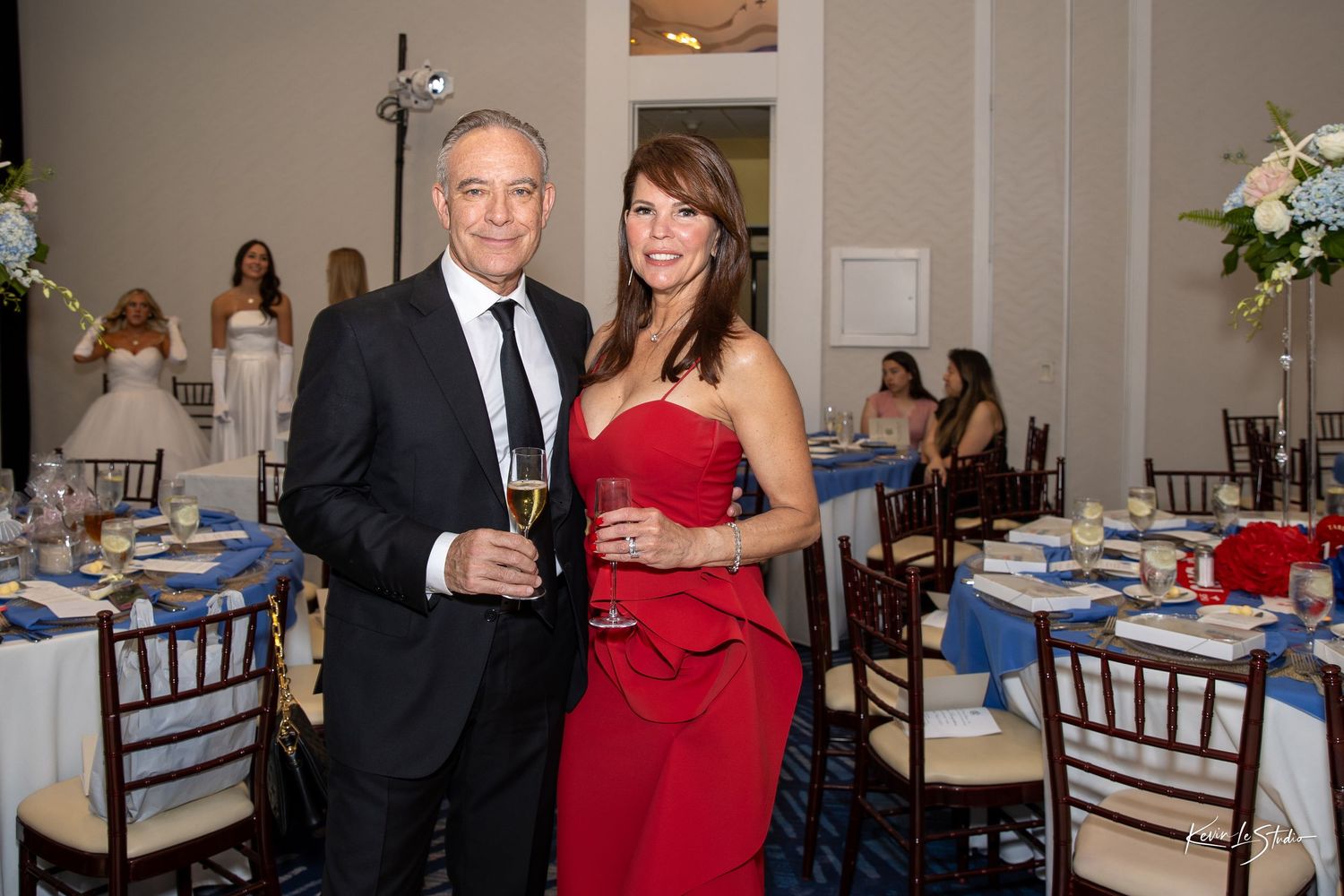 Formal event at an elegant venue with people gathered around tables decorated in blue and white linens.