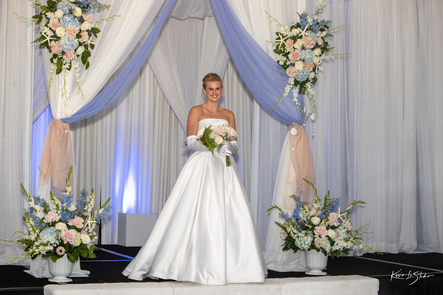 Wedding ceremony backdrop with white drapes, floral arrangements, and elegant lighting for a romantic celebration.