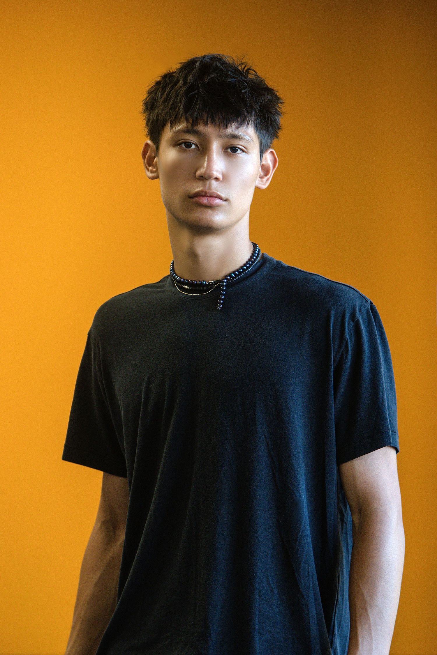 Portrait series of person wearing black t-shirt against vibrant orange background showing different poses and angles.