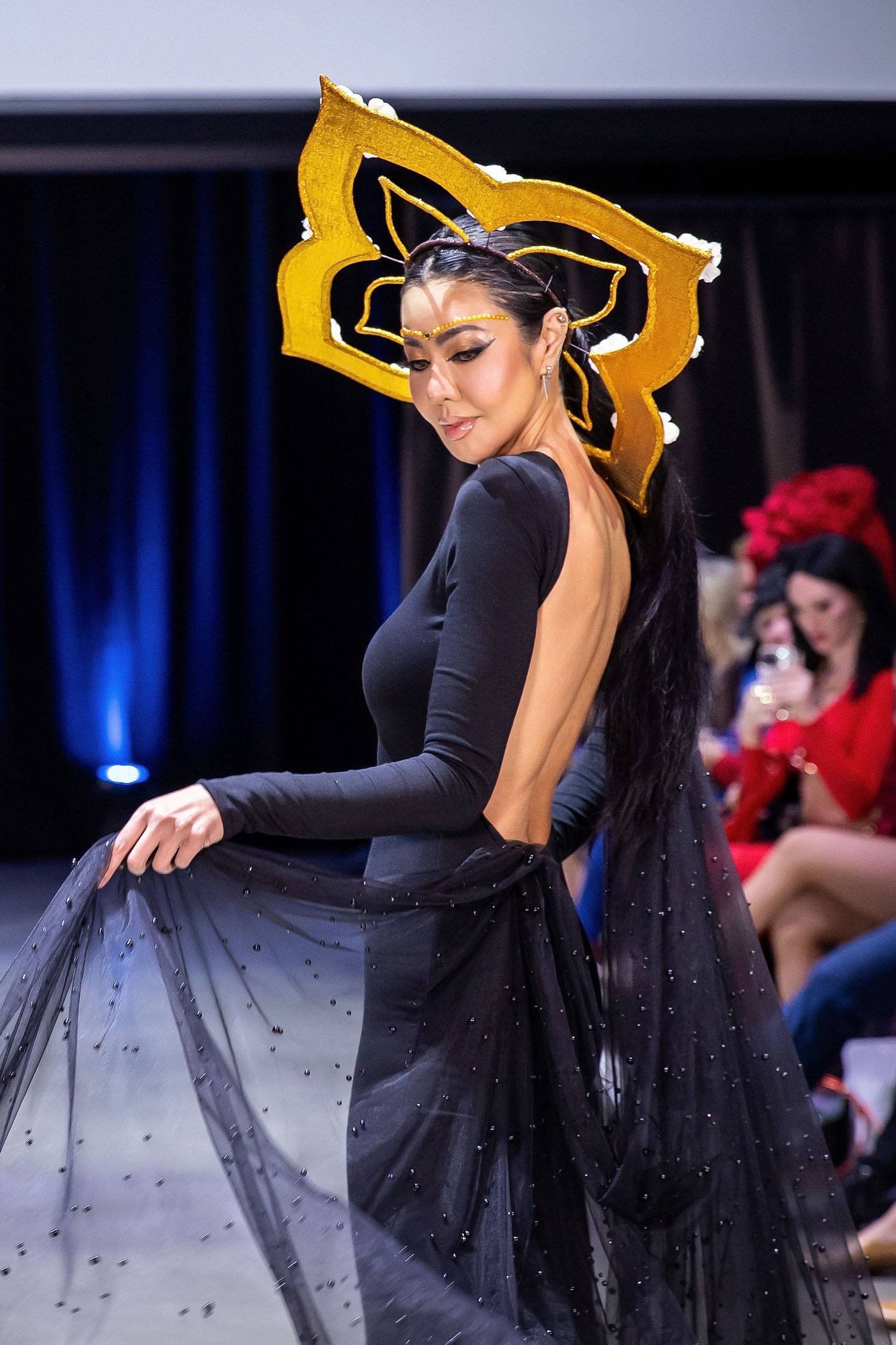 A dancer performs in a black dress with a flowing skirt and gold mask during a stage performance.