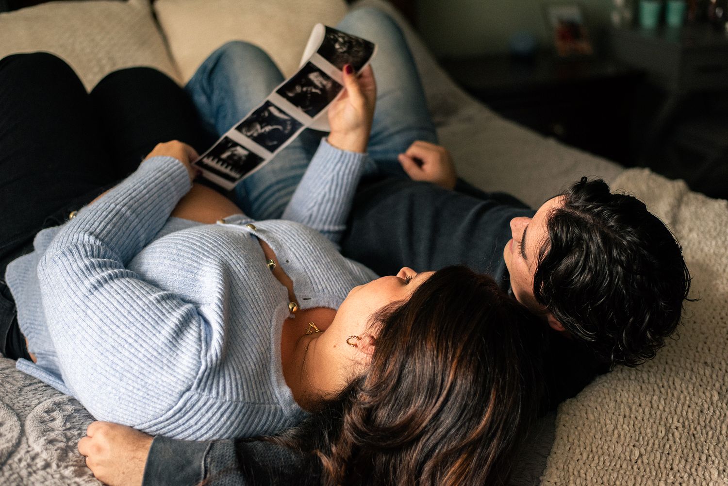 Couple lying down while looking at ultrasound photos together in a relaxed home setting.