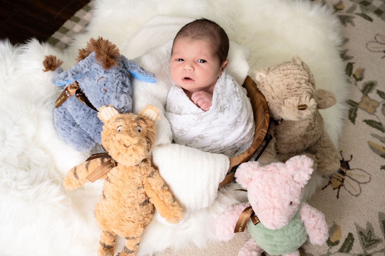 Baby lying on white fur rug surrounded by stuffed animal toys.