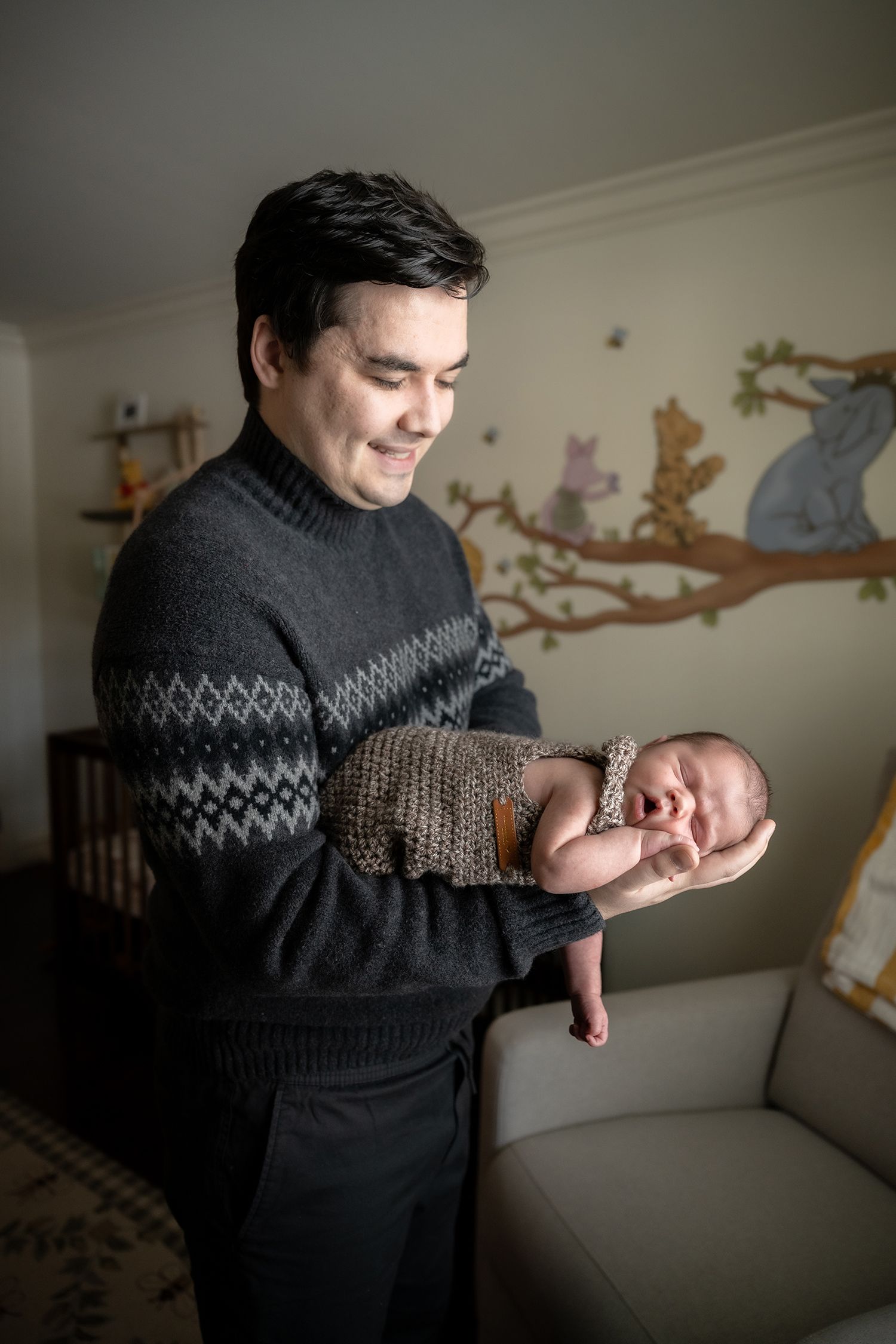 Person in dark patterned sweater holding small newborn baby against neutral background.