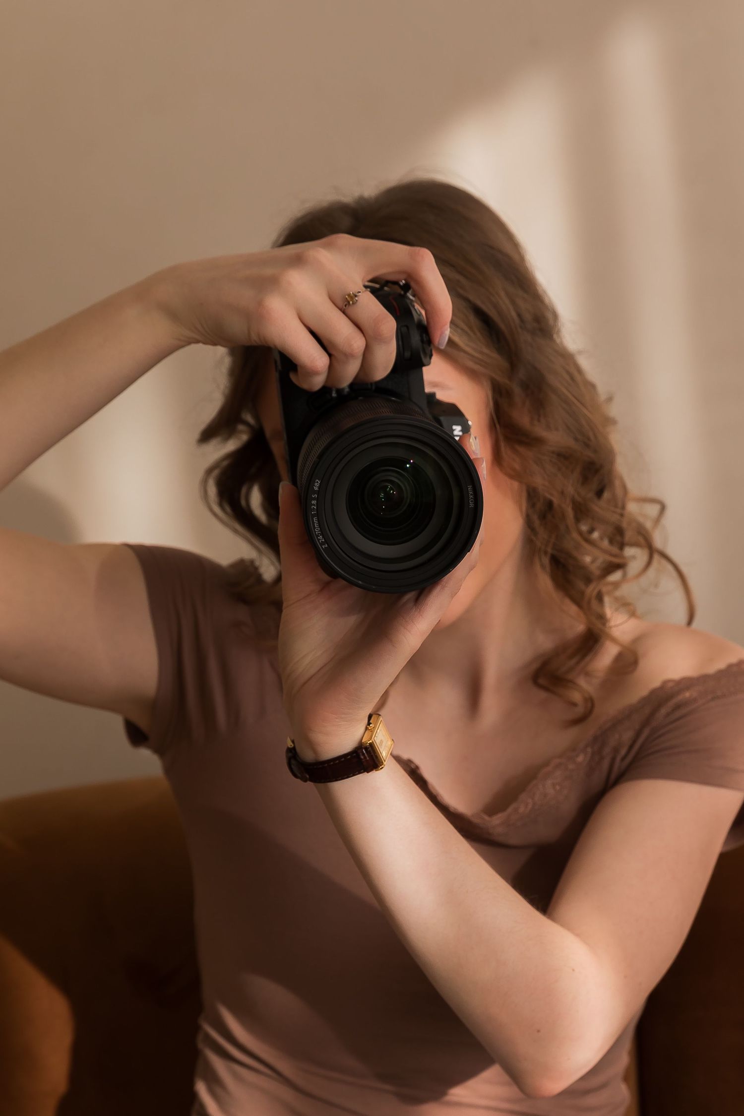 Photographer with curly hair holding professional camera in warm indoor lighting.