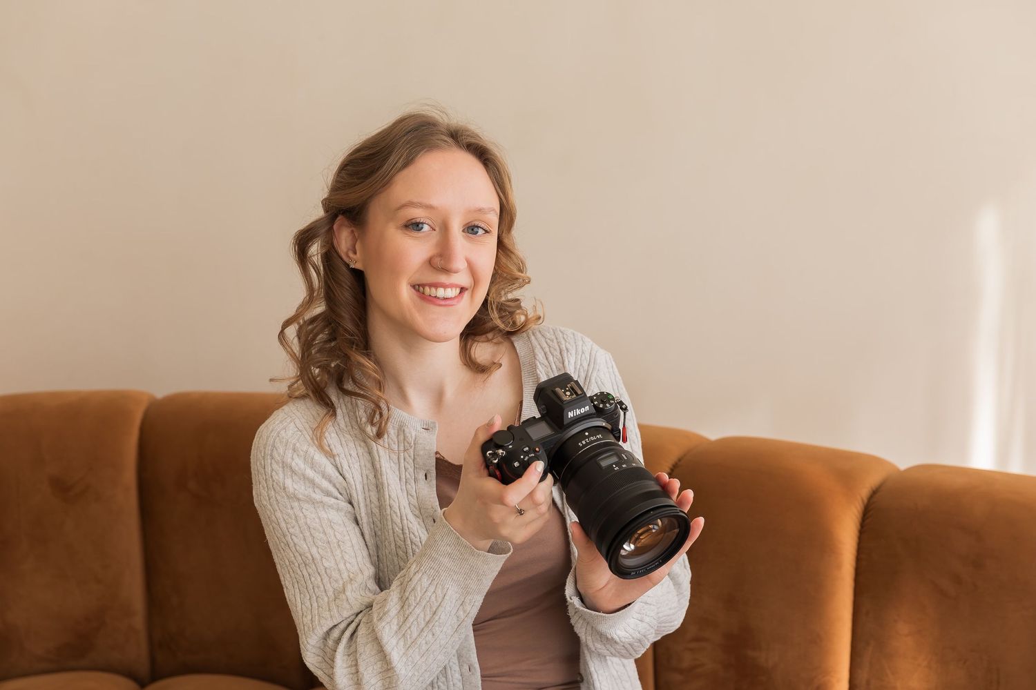 Person in gray sweater holding camera while sitting on brown leather couch.